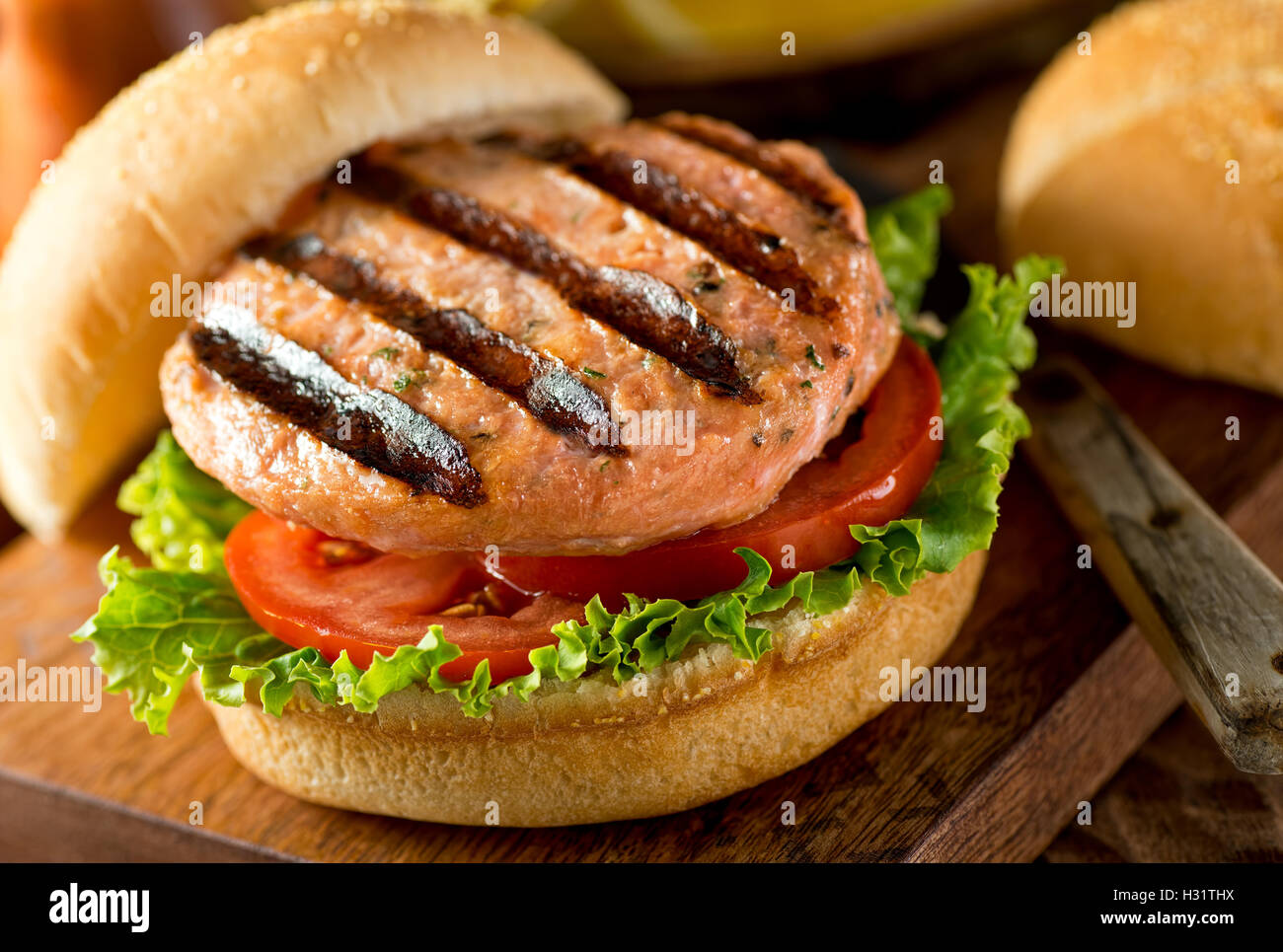 A delicious homemade grilled salmon burger with tomato and lettuce on a bun. Stock Photo