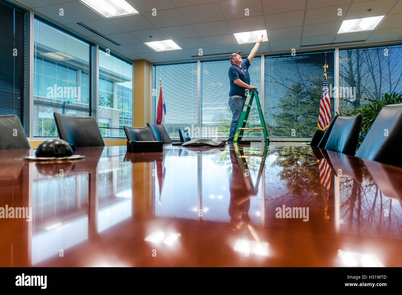 Maintenance man fixing a light in a conference room. Stock Photo