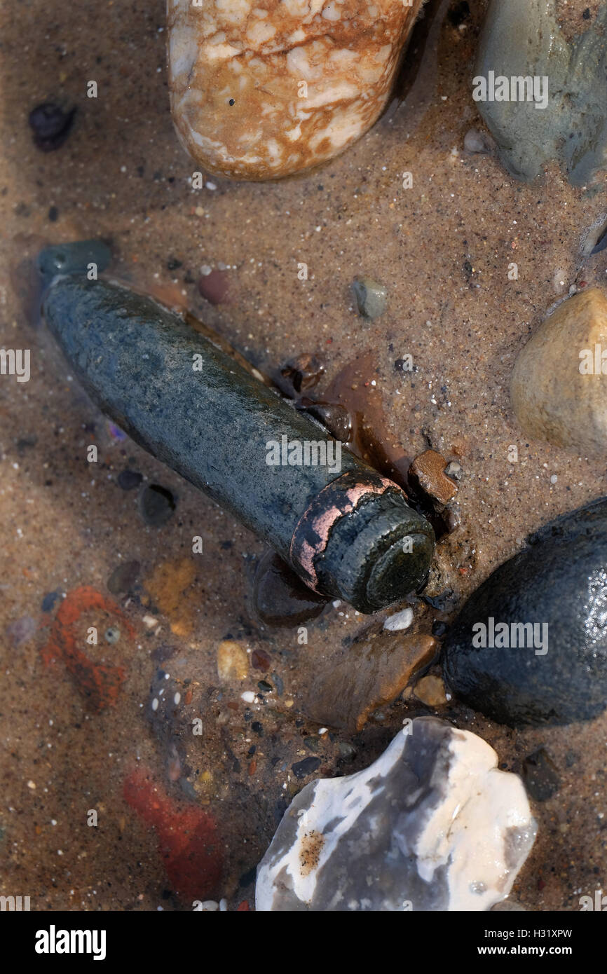 Spent world war two twenty millimeter cannon shells in wet sand on a beach. Stock Photo