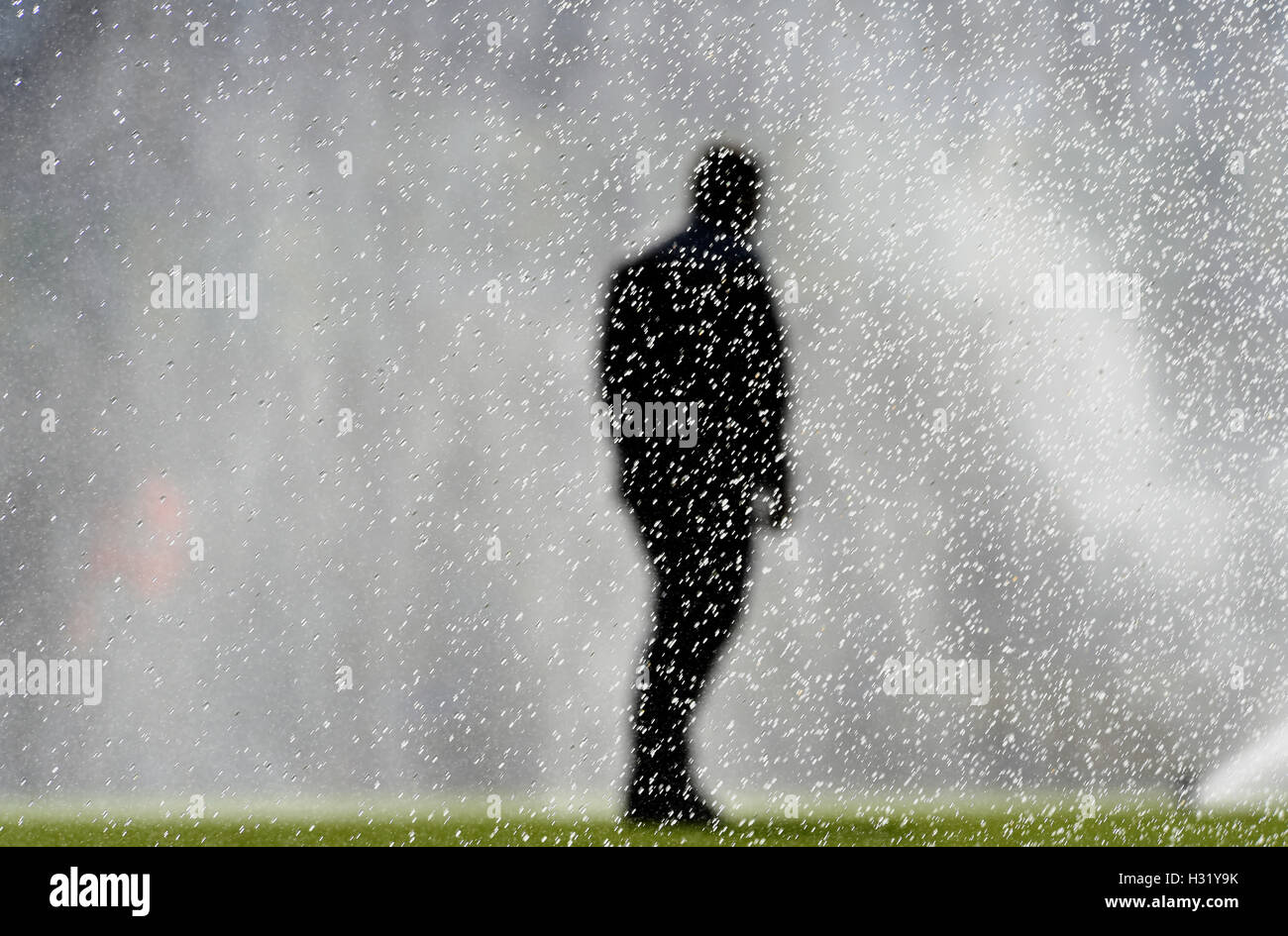 Sports field water sprinkler watering grass turf with ground staff silhouette figure Stock Photo
