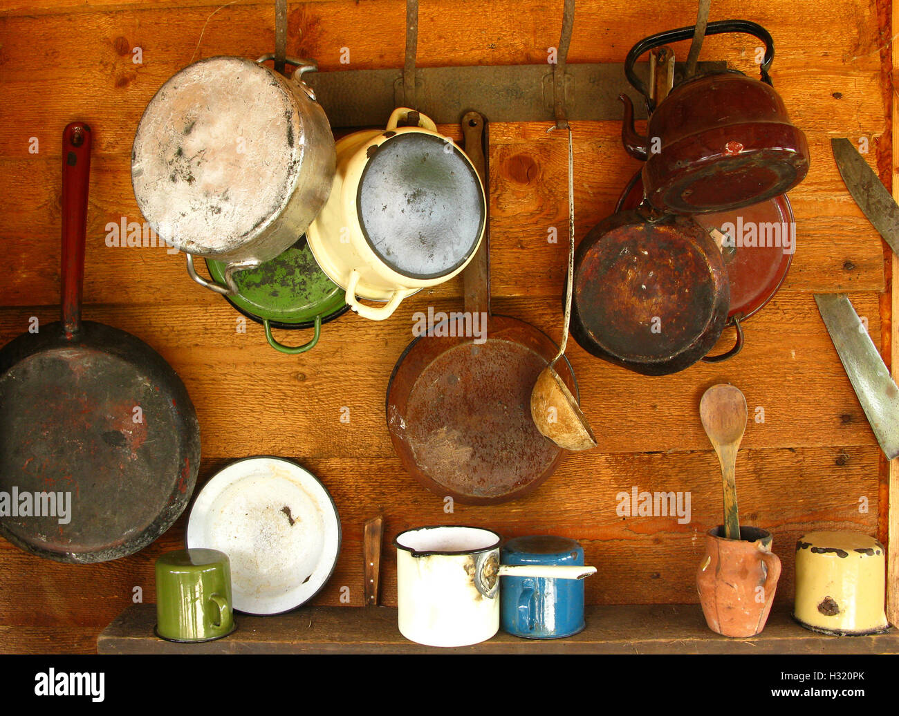 Scratched and damaged old frying pans and cooking pots hanging on a wooden wall Stock Photo