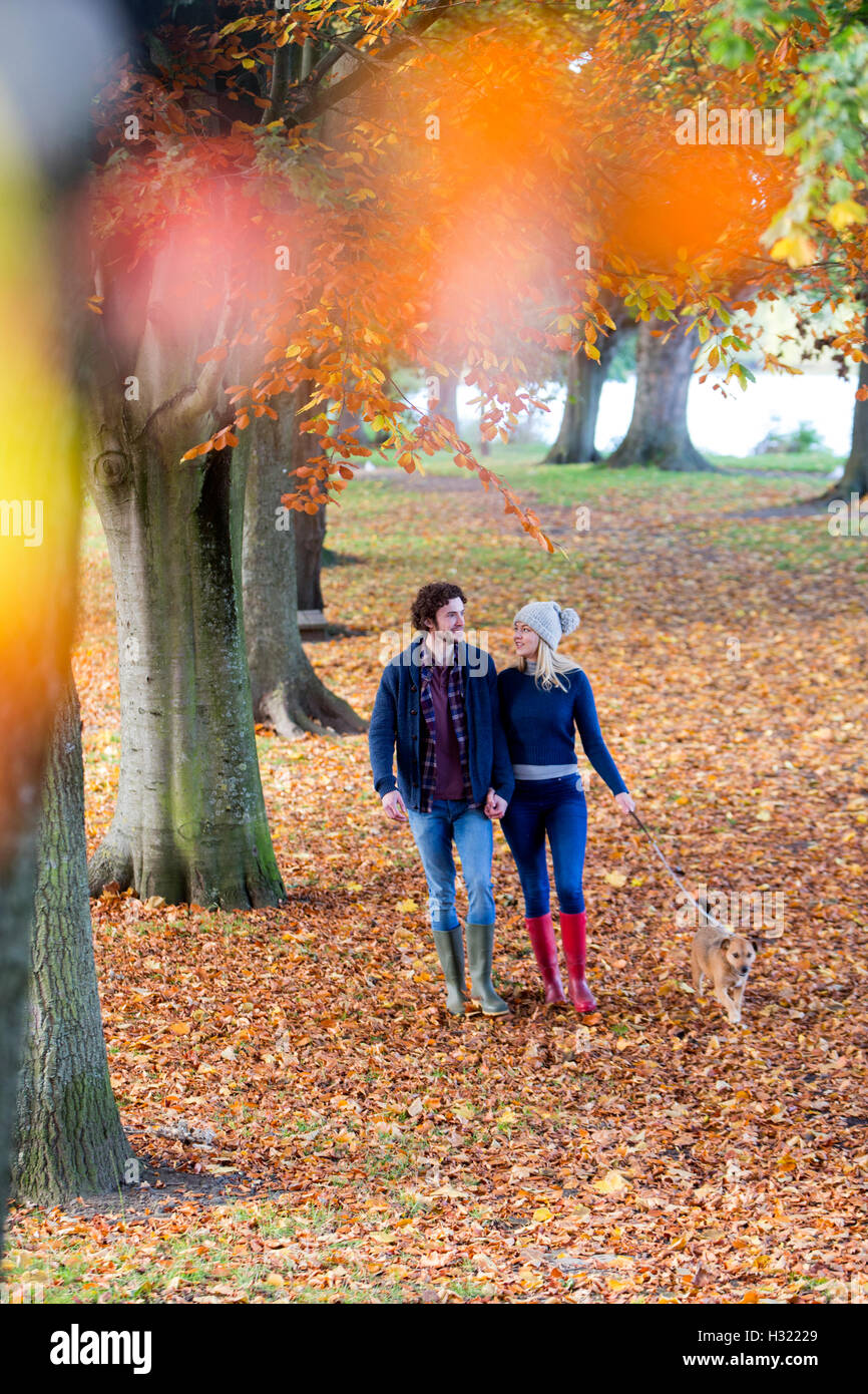Young couple enjoying a walk together in Autumn. They are hand in hand and talking as they stroll through the park with their pe Stock Photo