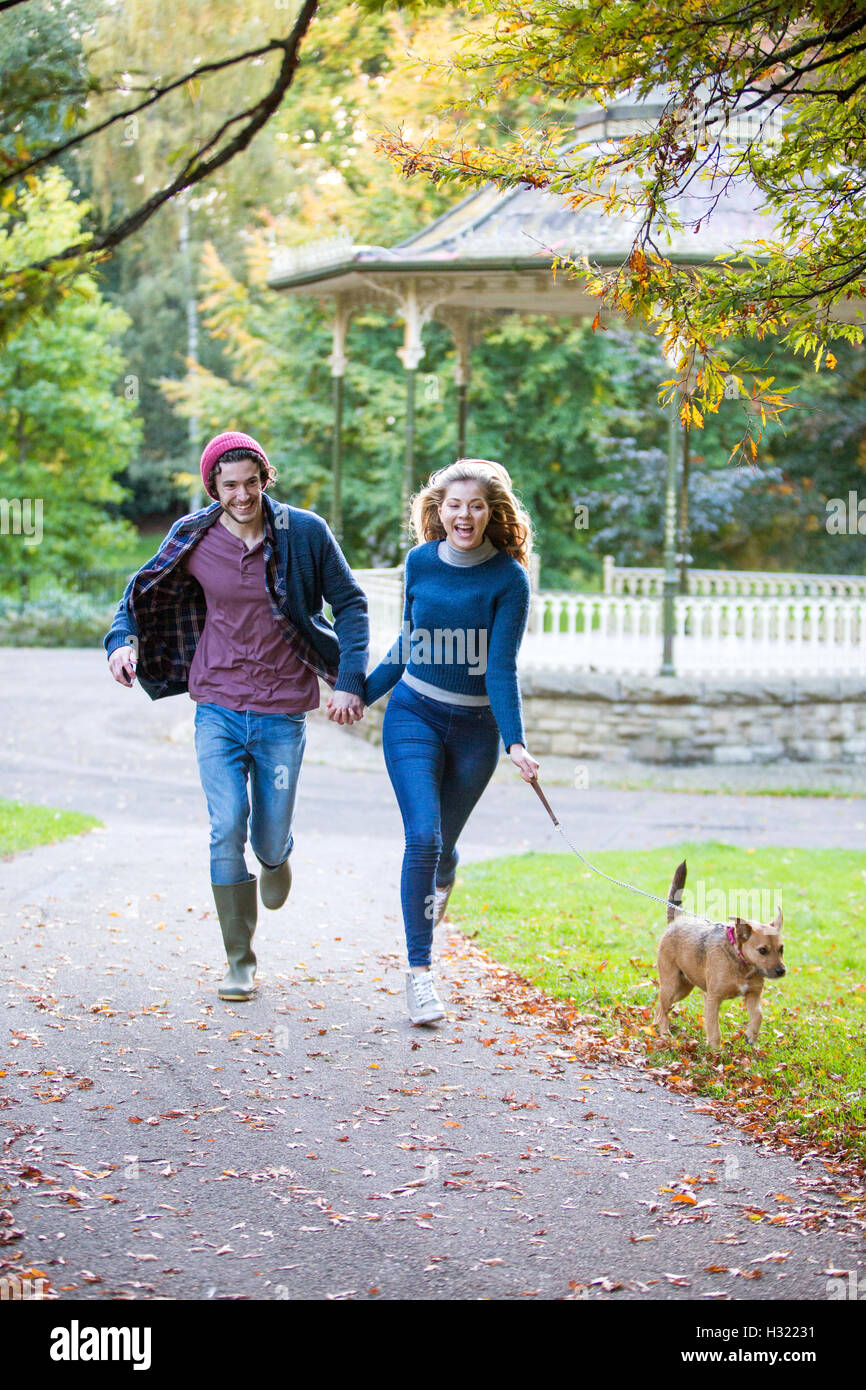Young couple running through the park with their pet dog Stock Photo ...