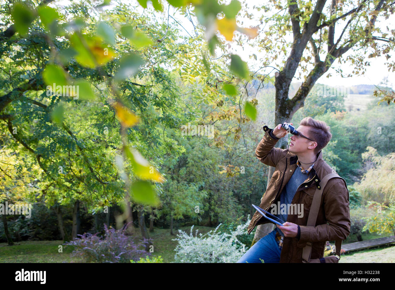 Young man analysing nature with binoculars. He is using a digital tablet for research. Stock Photo