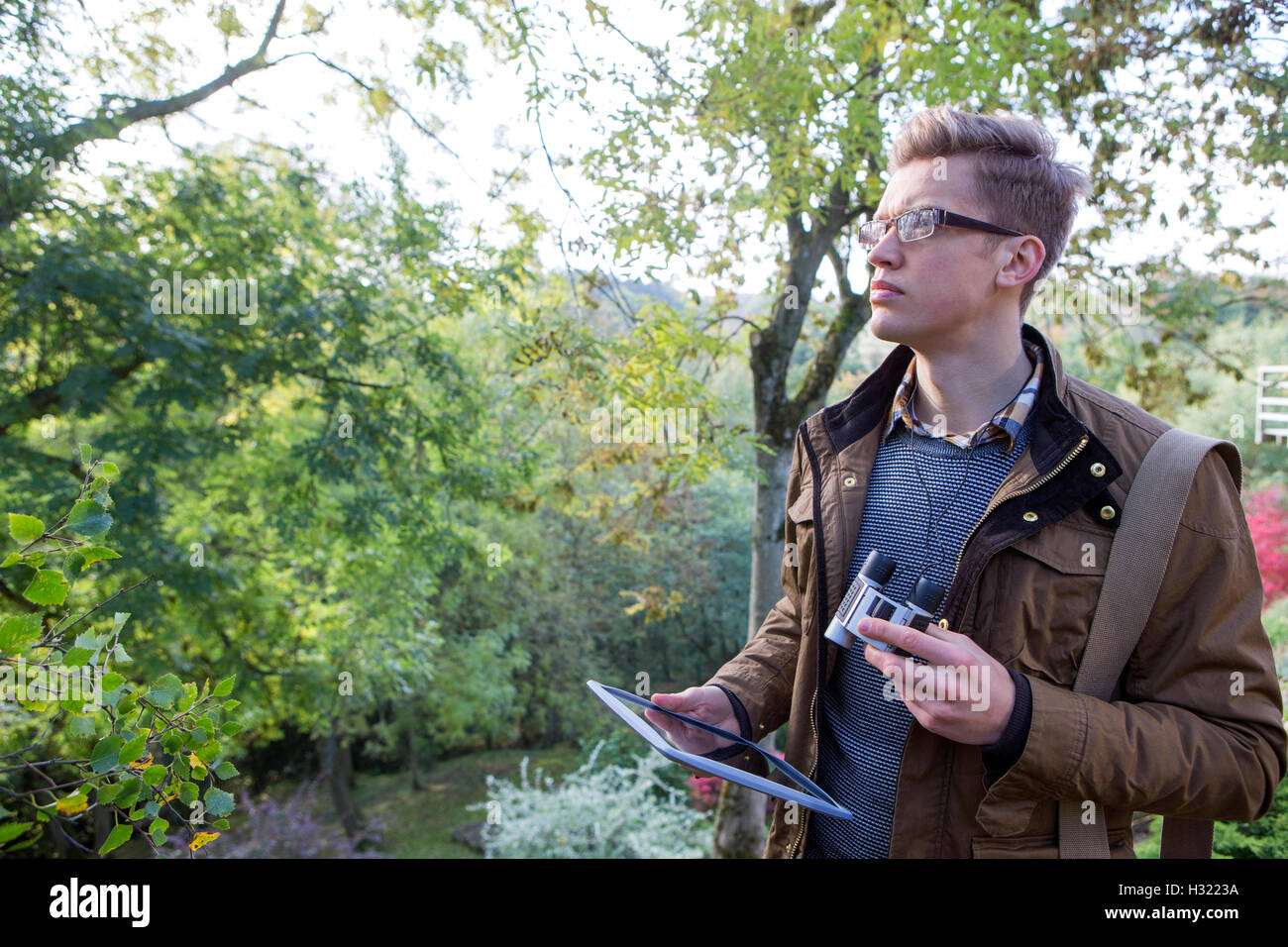 Young man analysing nature with binoculars. He is using a digital tablet for research. Stock Photo