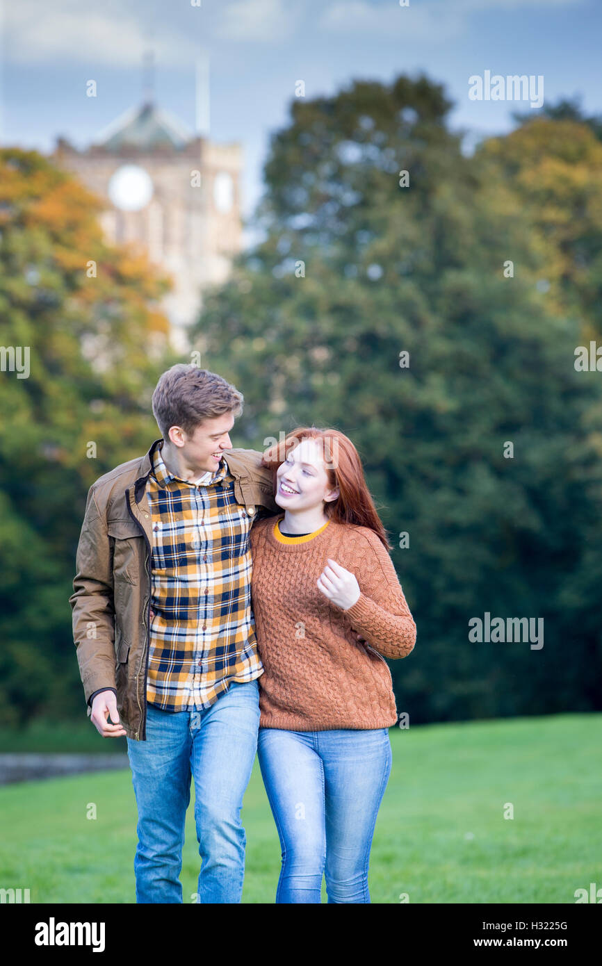 Young couple walking and talking in a park. They have their arms round each other and are looking at each other. Stock Photo