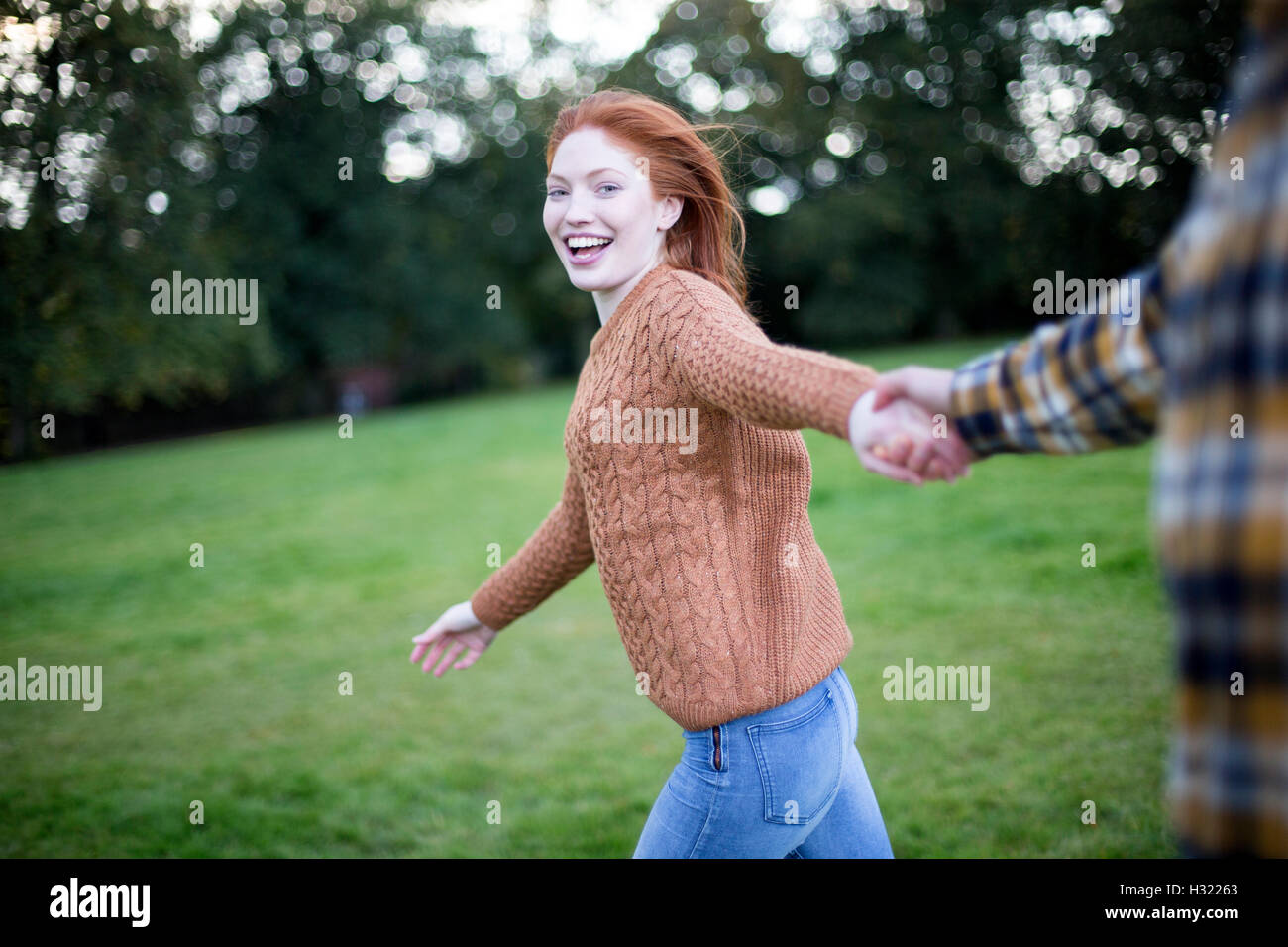 Point of view shot of a young woman running whilst holding her partners hand. She is looking at the camera. Stock Photo