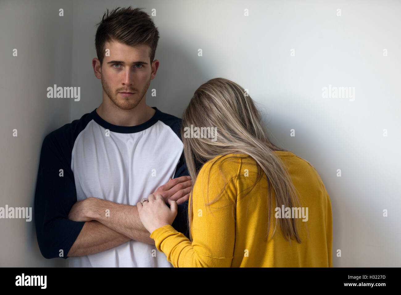 Young woman crying on her partners shoulder. He is looking at the camera with his arms folded. Stock Photo