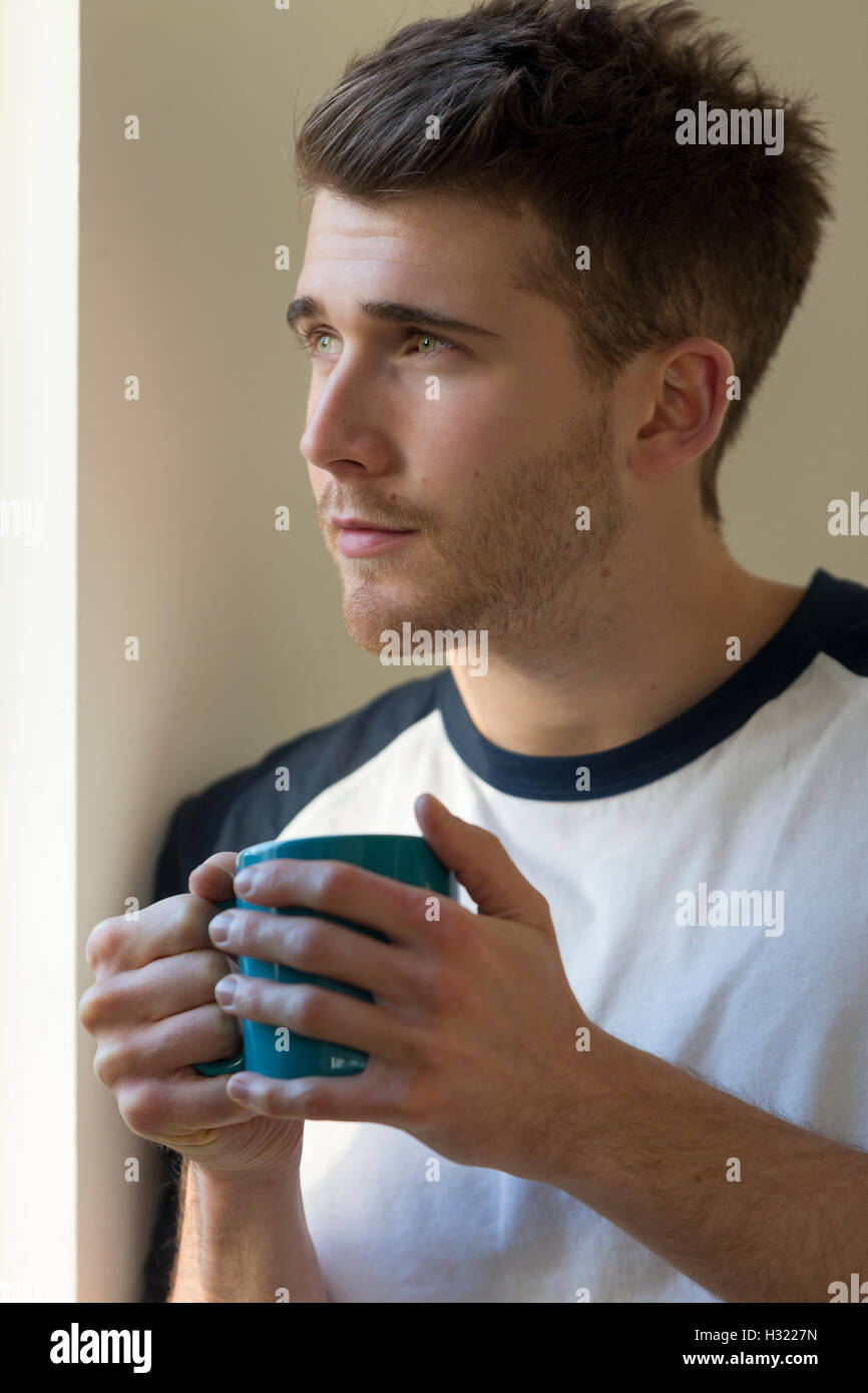 Portrait of a man looking out a window with a hot drink in his hands. Stock Photo