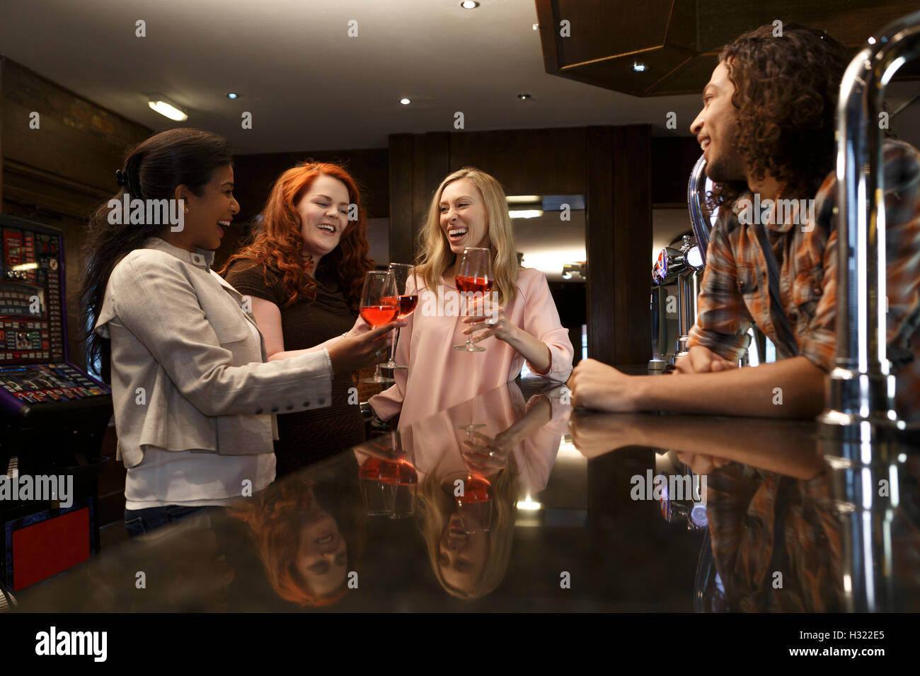 Three women making a toast with glasses of red wine at a bar. Stock Photo