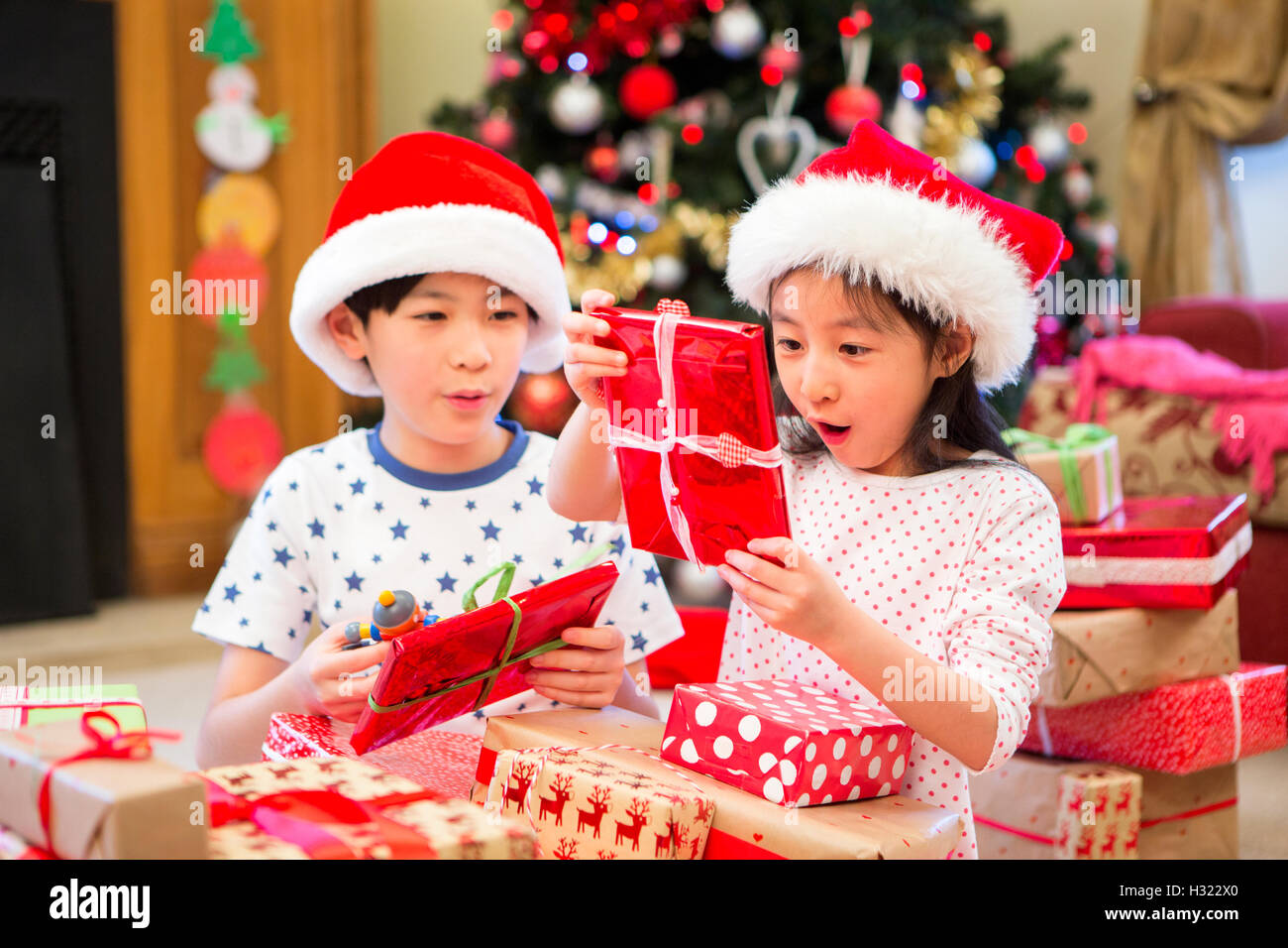 Chinese siblings sitting together on the floor in their living room on Christmas morning. They are opening presents with excited Stock Photo