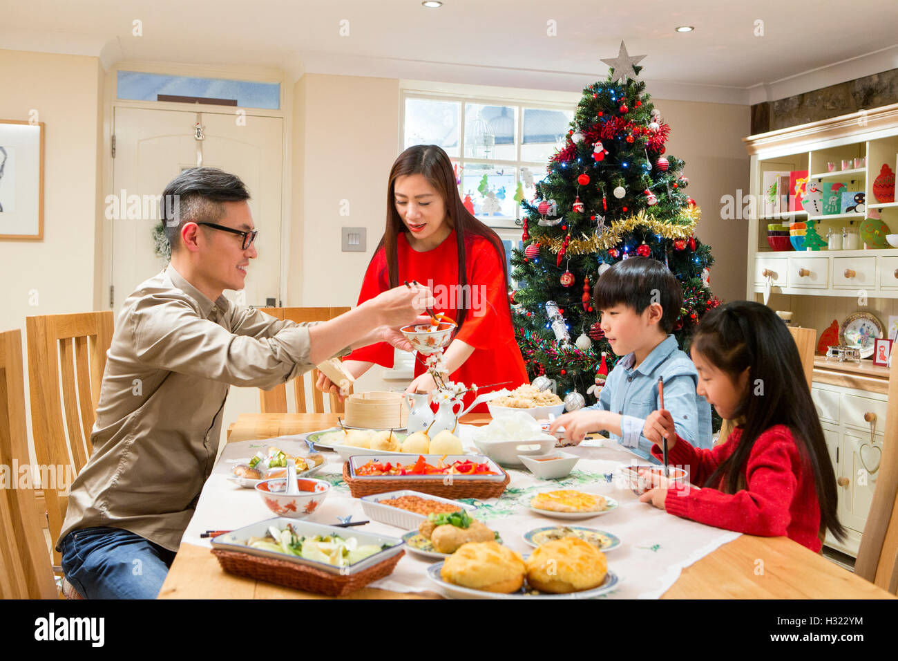 Chinese family enjoying their christmas dinner. They are eating traditional Chinese food. The parents are serving it round the t Stock Photo