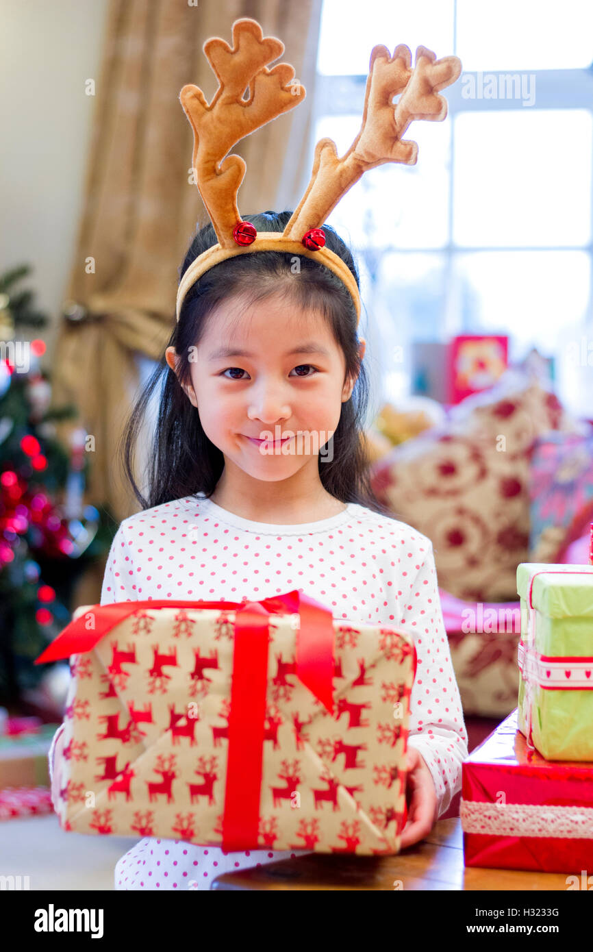 Cute Chinese girl wearing festive antlers. She is holding a present up and looking at the camera with a cheeky smile on her face Stock Photo