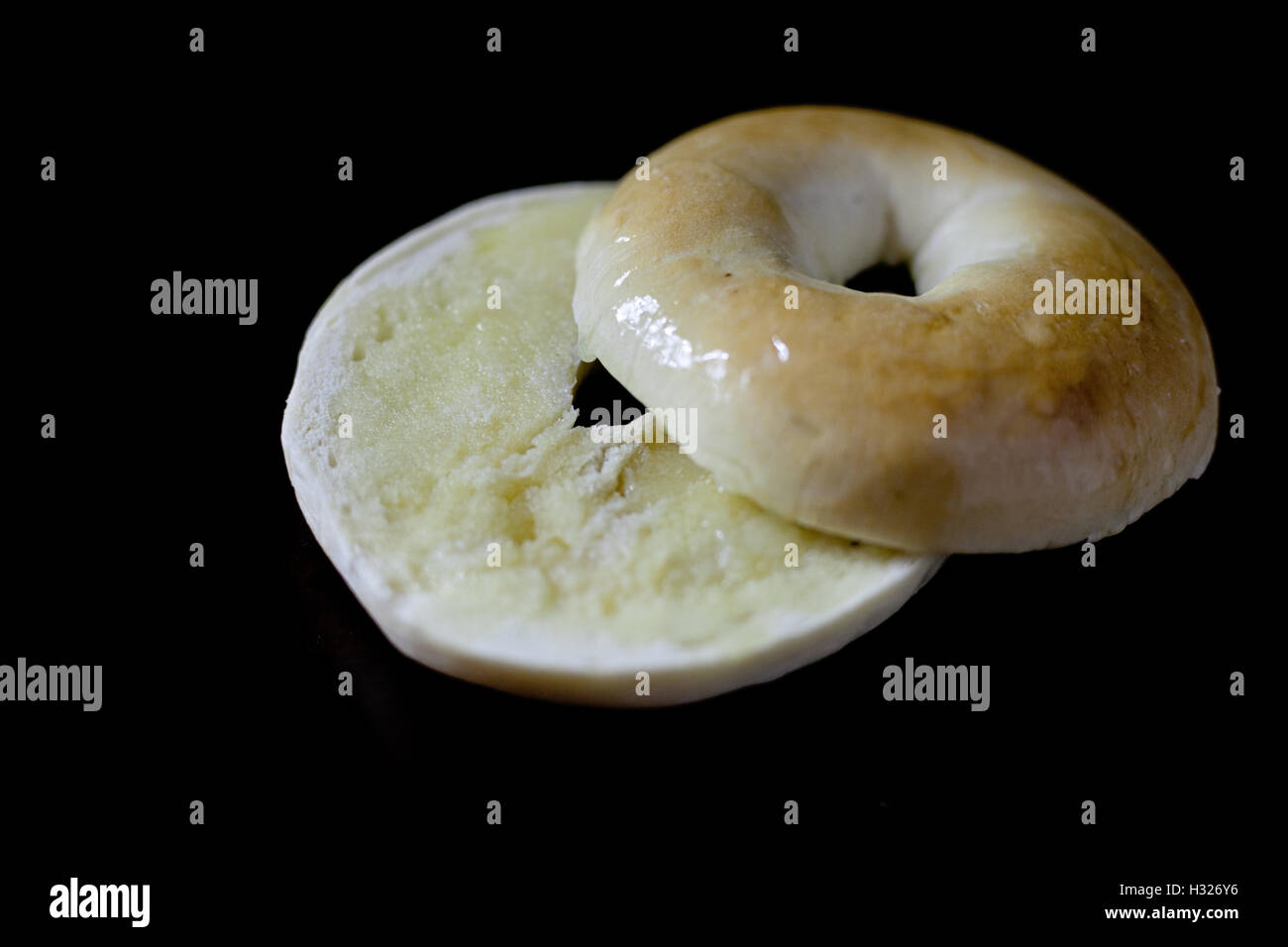 A bagel that has been cut in half and buttered on a black background