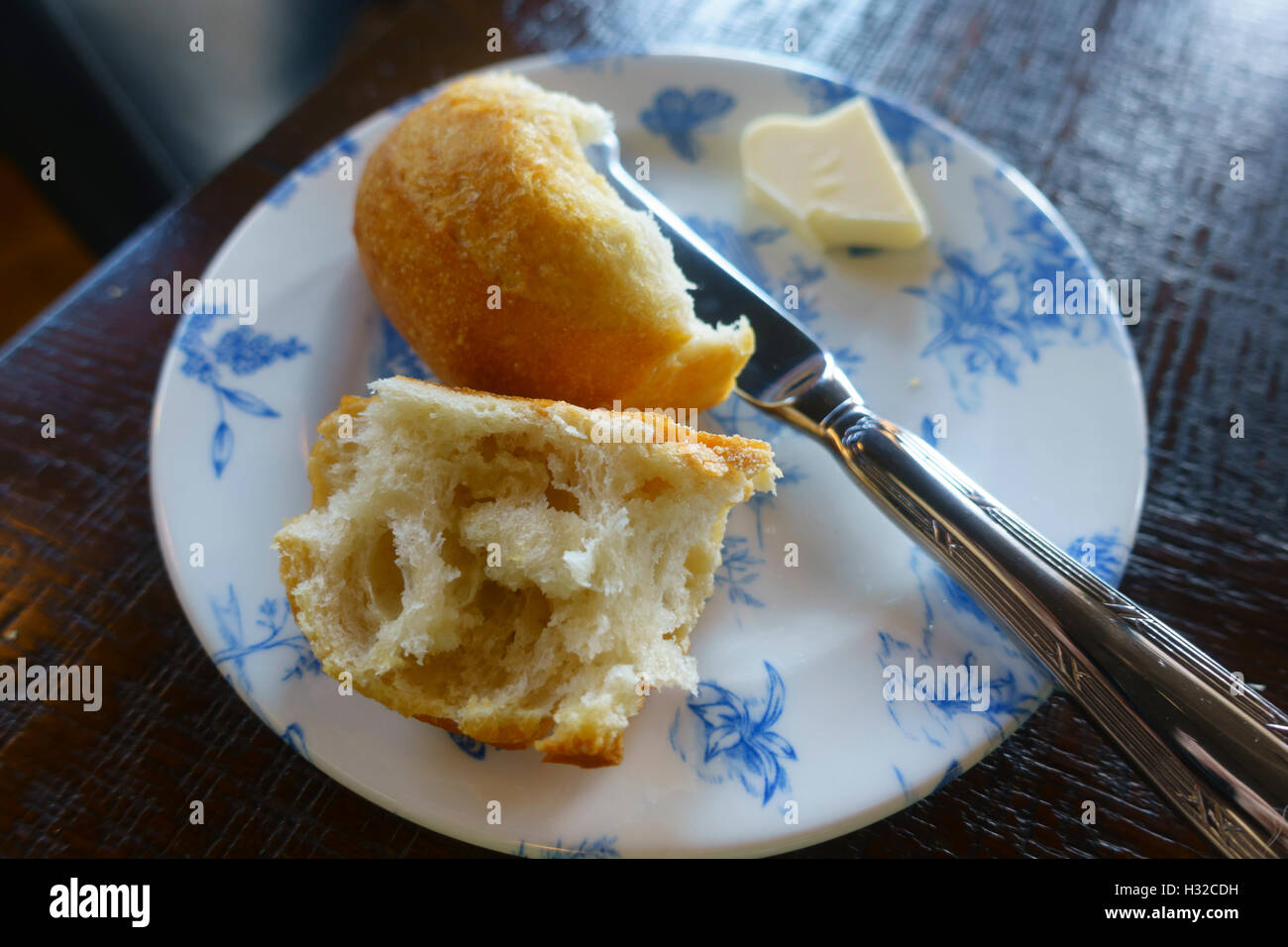 Crusty white roll with knife and butter on a blue and white plate Stock Photo