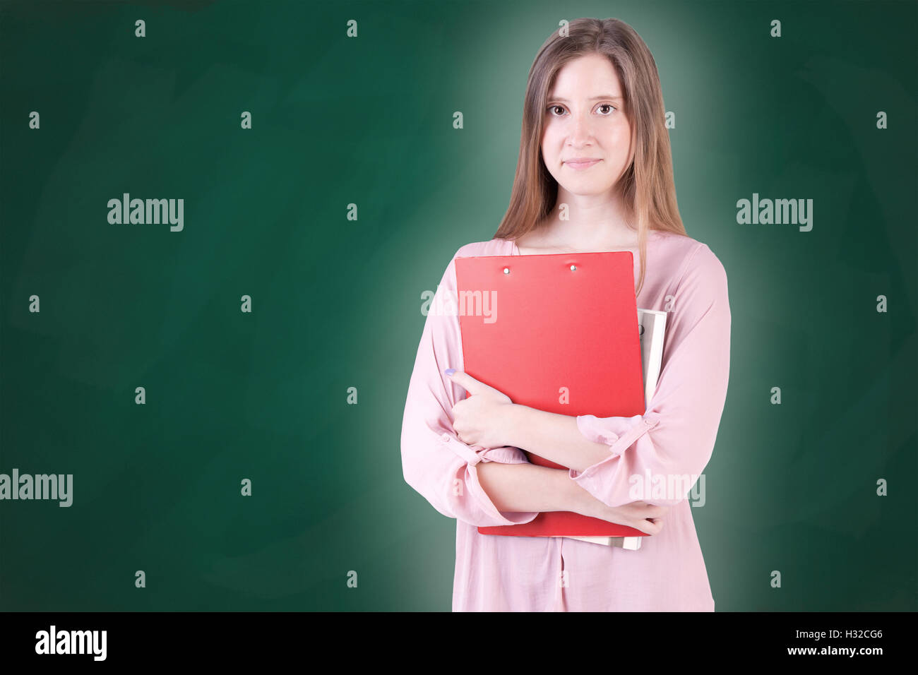 Young woman carrying notebooks in her arms, in a green chalkboard background Stock Photo