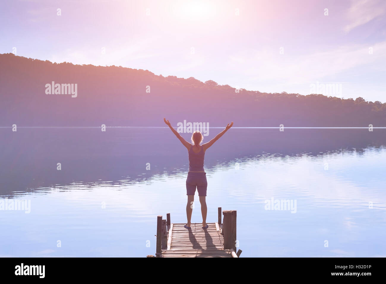 Happy woman raising hands in sign of success and facing the morning sunrise light Stock Photo