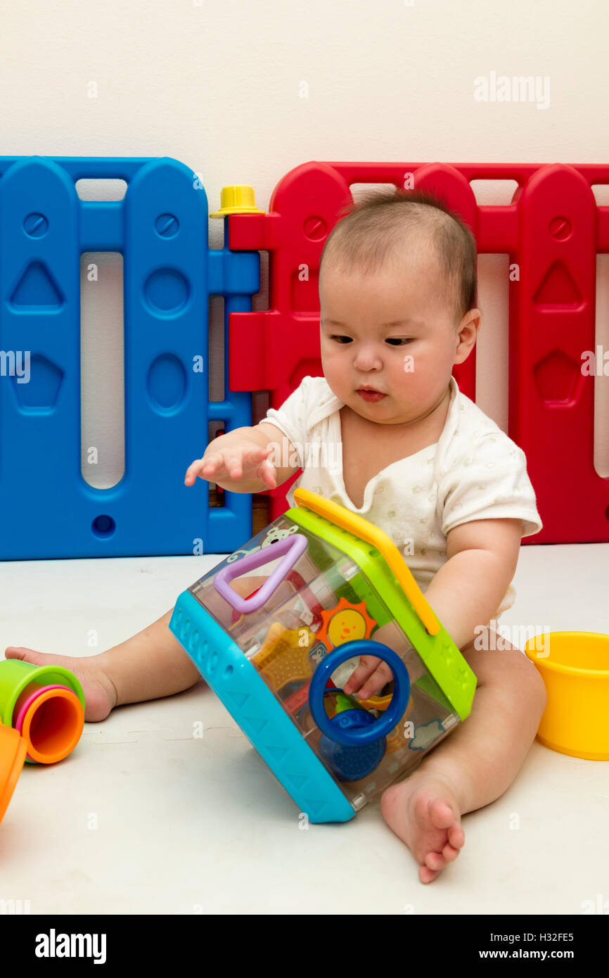 baby playing with Fisher Price Peek-A-Blocks Shape Sorter in playpen Stock Photo