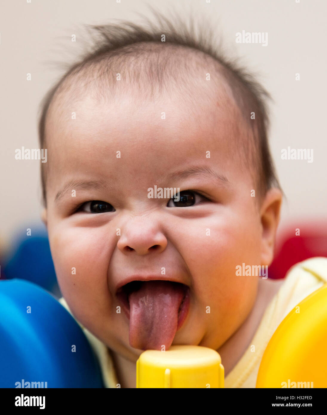 baby with funny grin licking plastic post in playpen Stock Photo