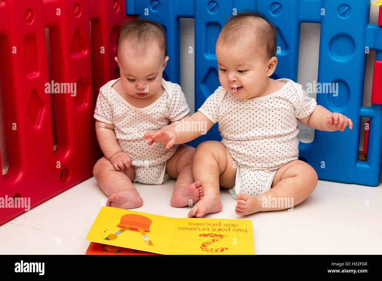 twin babies looking at picture book in playpen Stock Photo