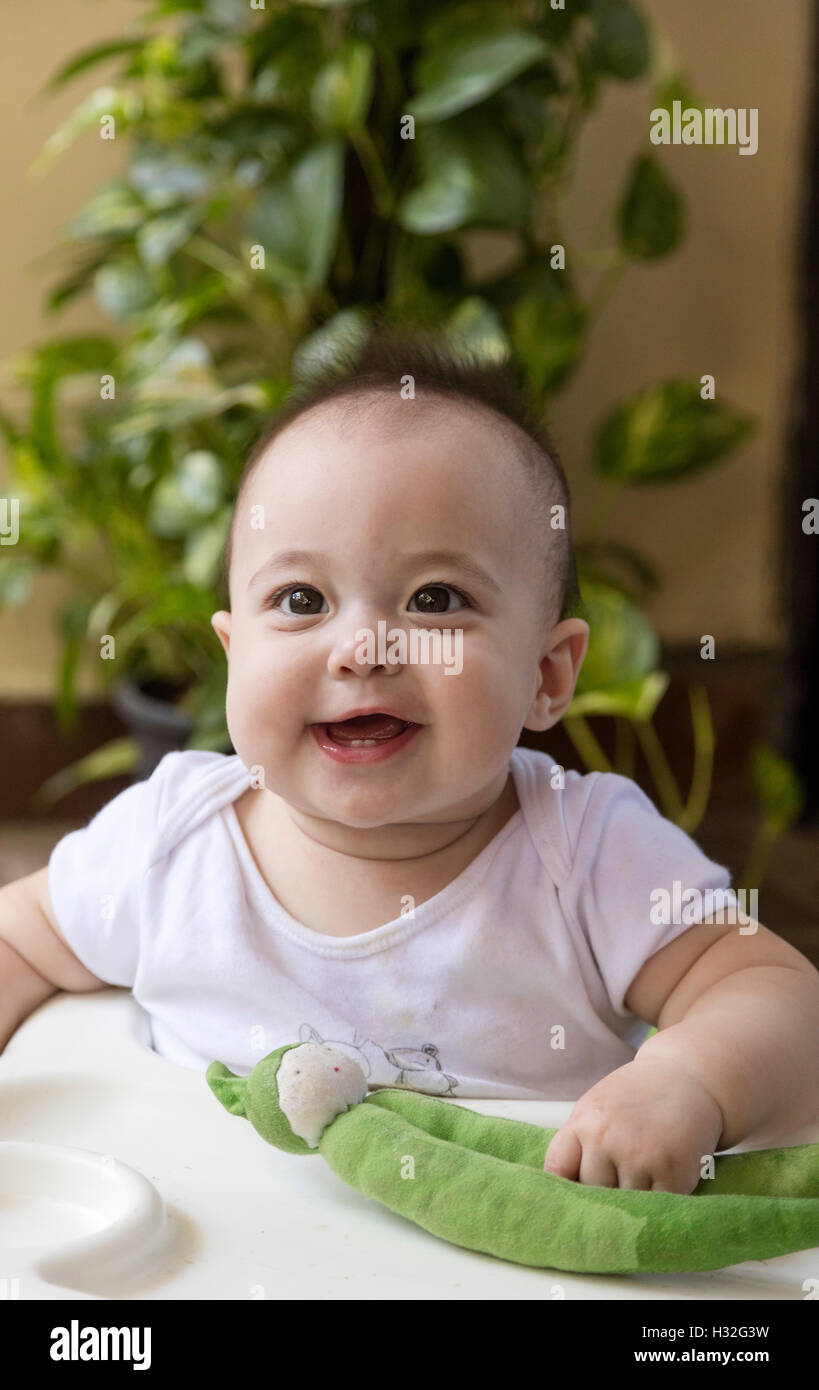 smiling baby holding bean toy  with vegetation in background Stock Photo