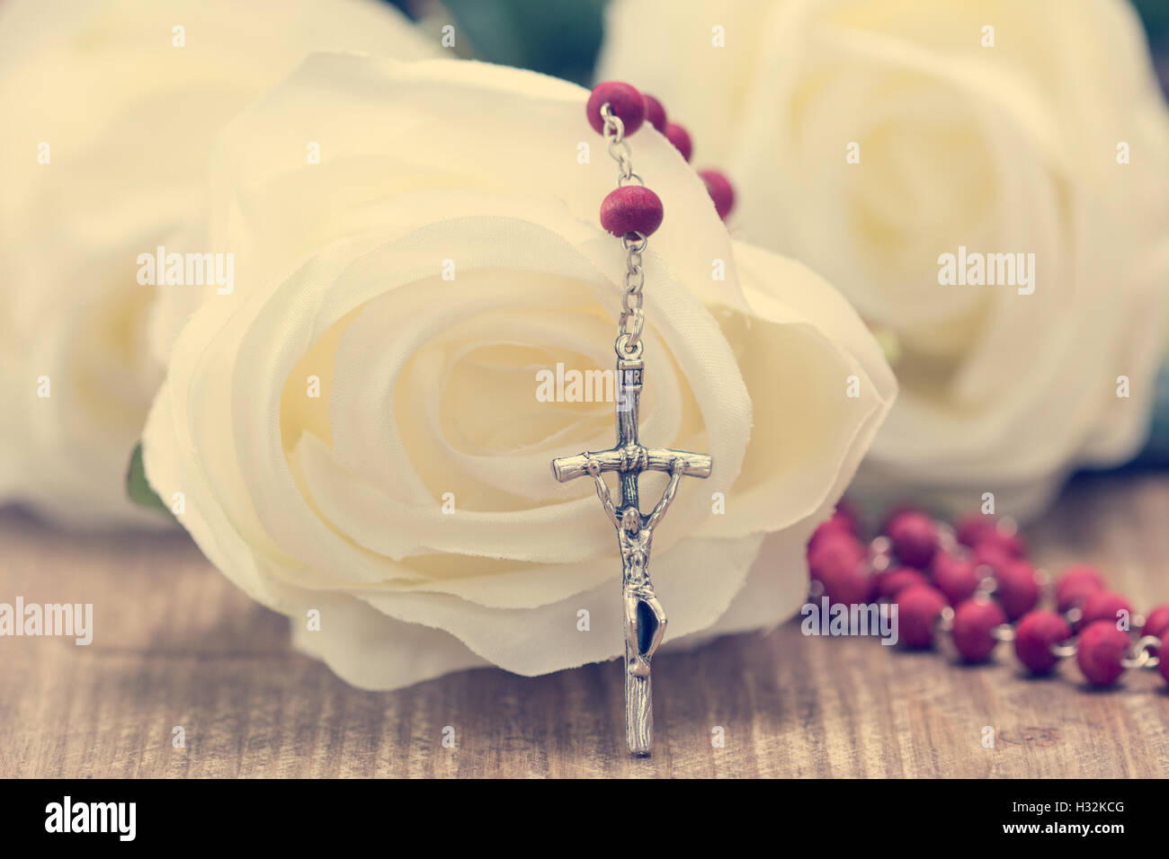 Catholic rosary and white roses on wooden background. Religion concept