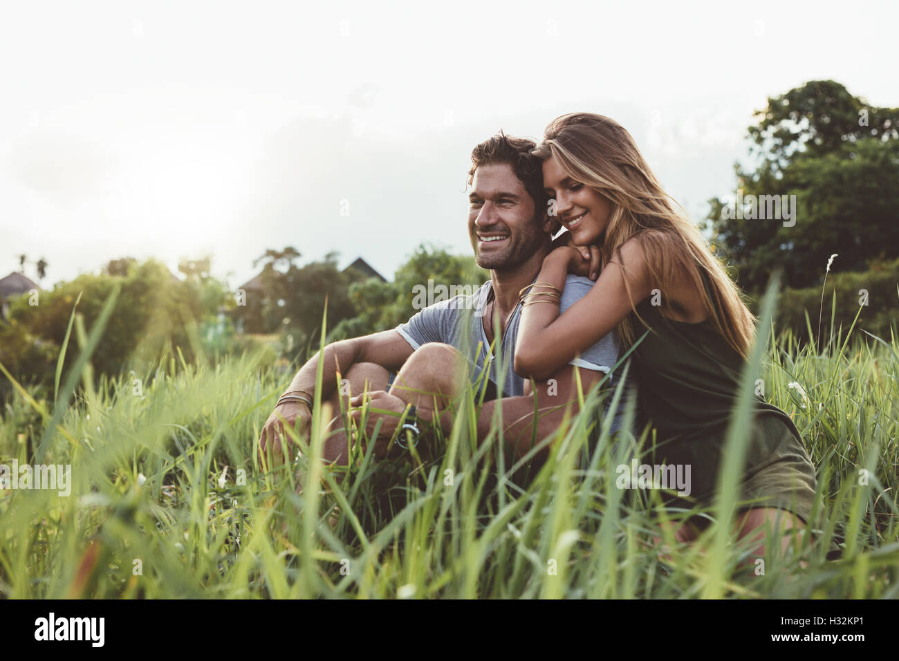 Outdoor shot of young happy lovers sitting on meadow. Happy young couple in grass. Stock Photo