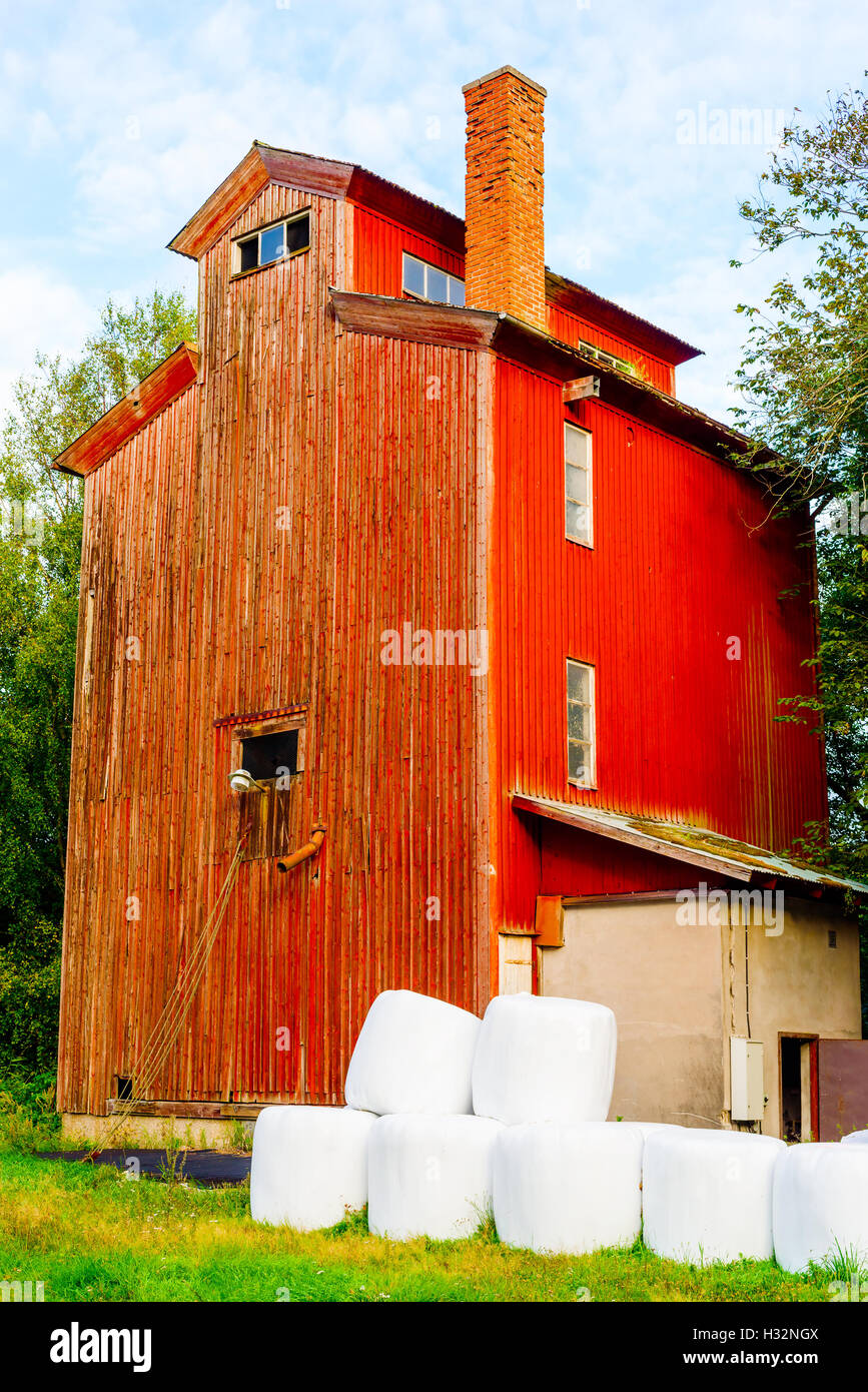 Red wooden storage building or vintage farmhouse with white silage bales in front. Stock Photo