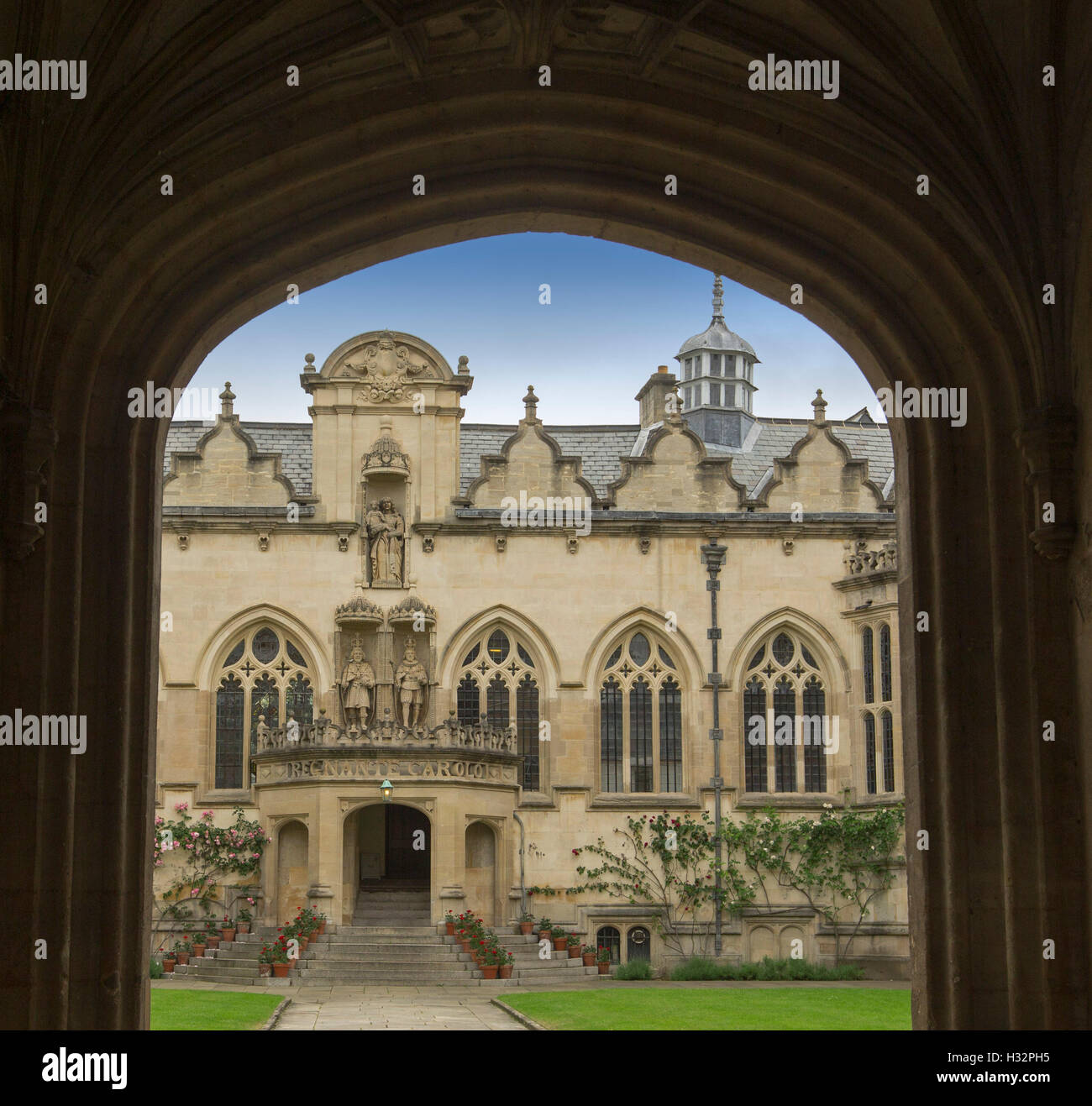 Ornate entrance to Oriel college in Oxford, with  view through dark archway to 17th century gothic style building under blue sky Stock Photo