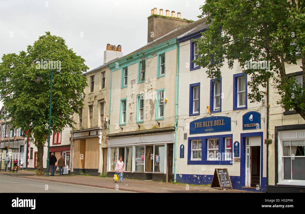 Main street of town of Egremont with shoppers walking past colourful but run down shops with flaking paint inCumbria, England Stock Photo