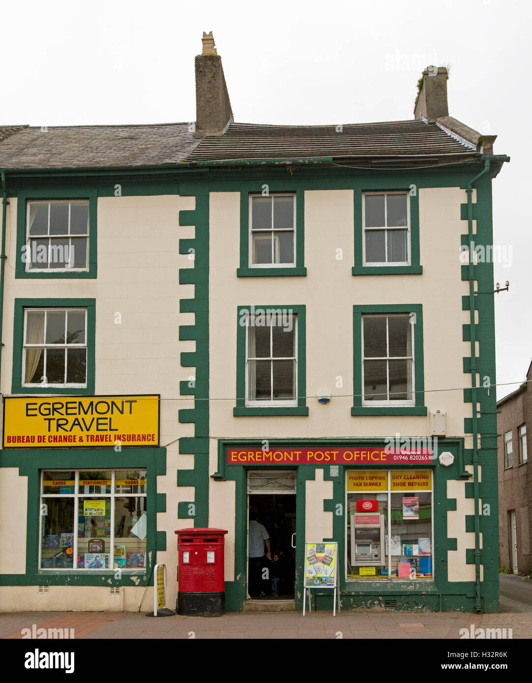 Old post office and adjacent shop, three stories high, painted green and cream, in main street of English town of Egremont Stock Photo
