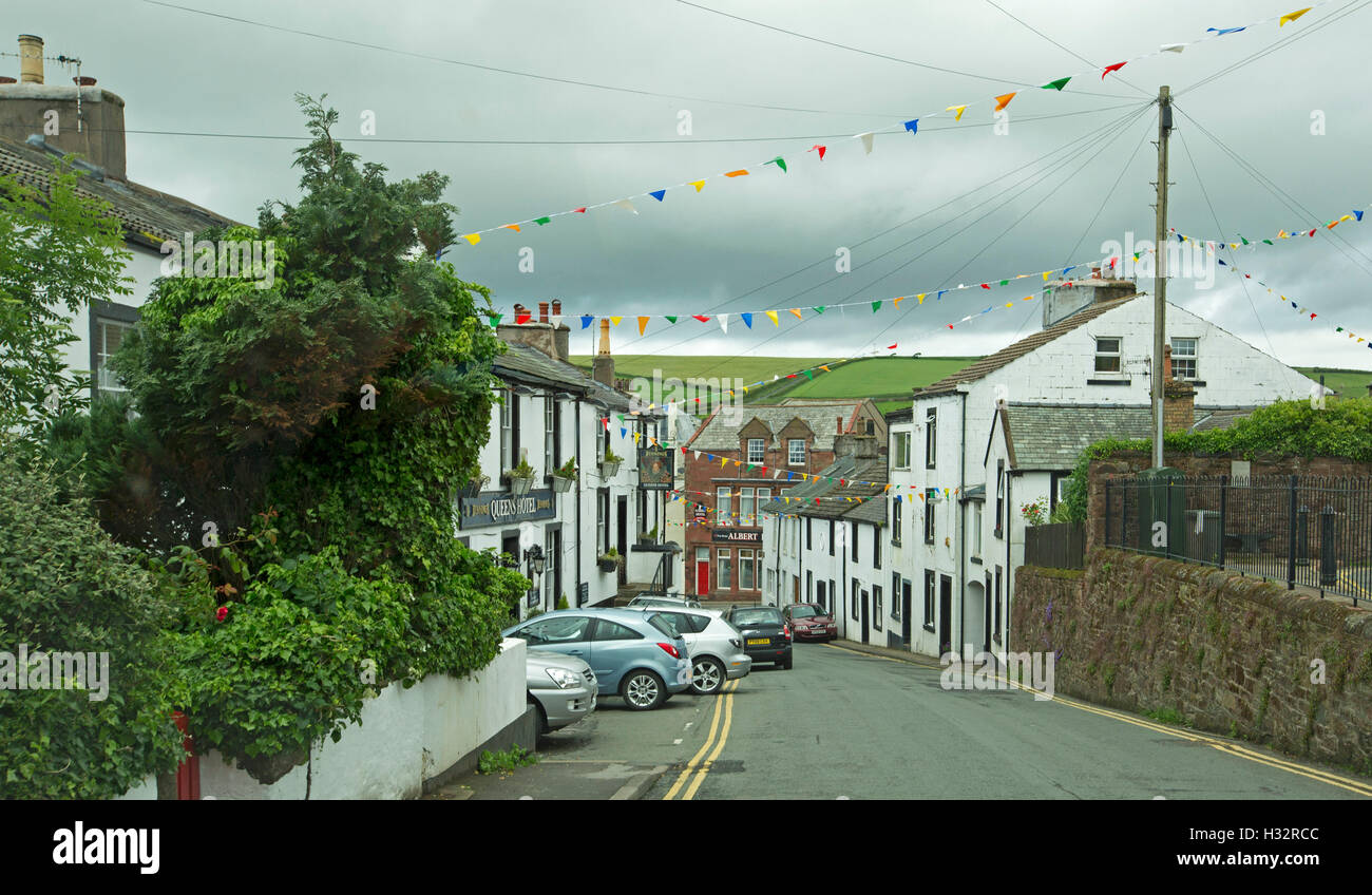 Coastal town of St Bees with street lined with white painted cottages and old stone wall & rolling green hills in background Stock Photo