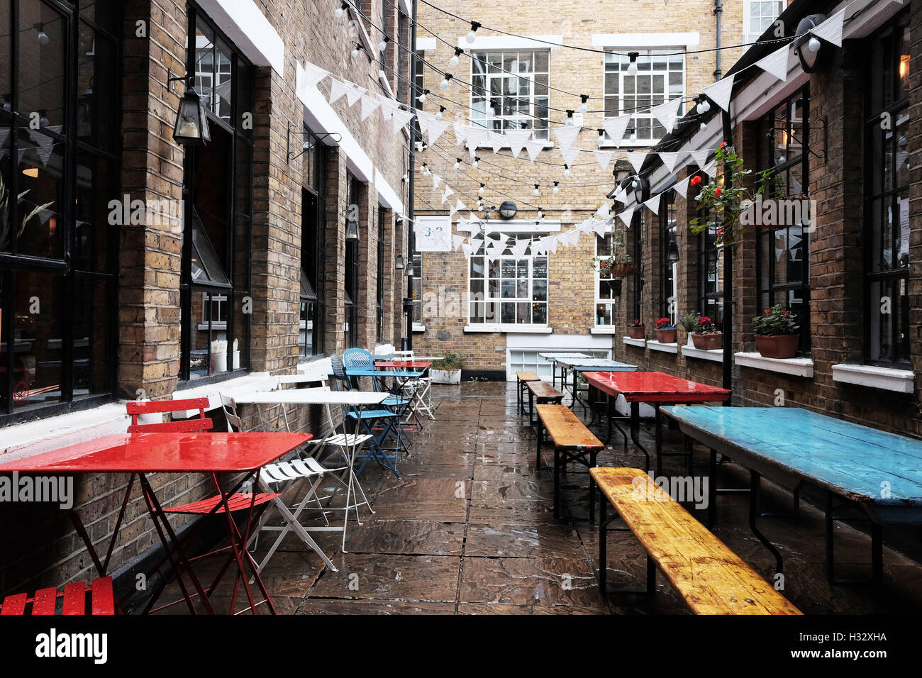 Café seating surrounded by brick walls with colourful tables and bunting in the rain. Stock Photo