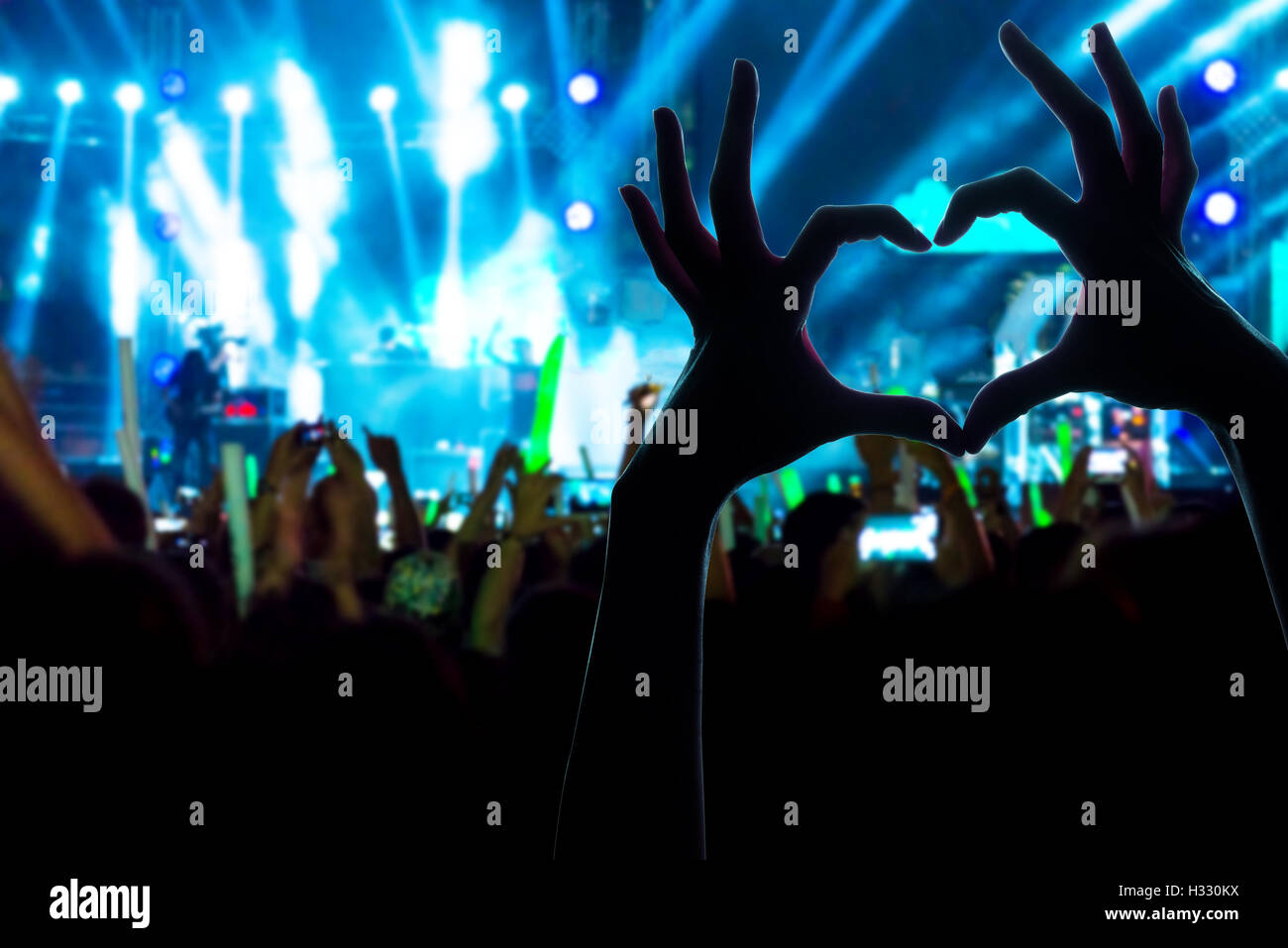 Festival crowd raising hands in music concert front of bright stage ...