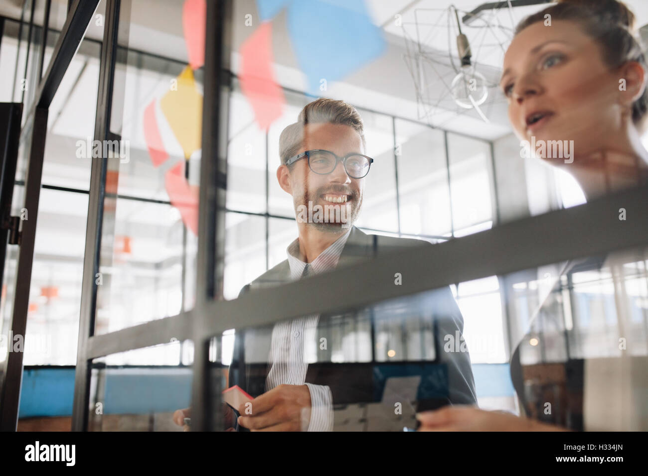 Two professional coworkers discussing new ideas on a glass wall. Creative professionals standing at the office behind glass wall Stock Photo