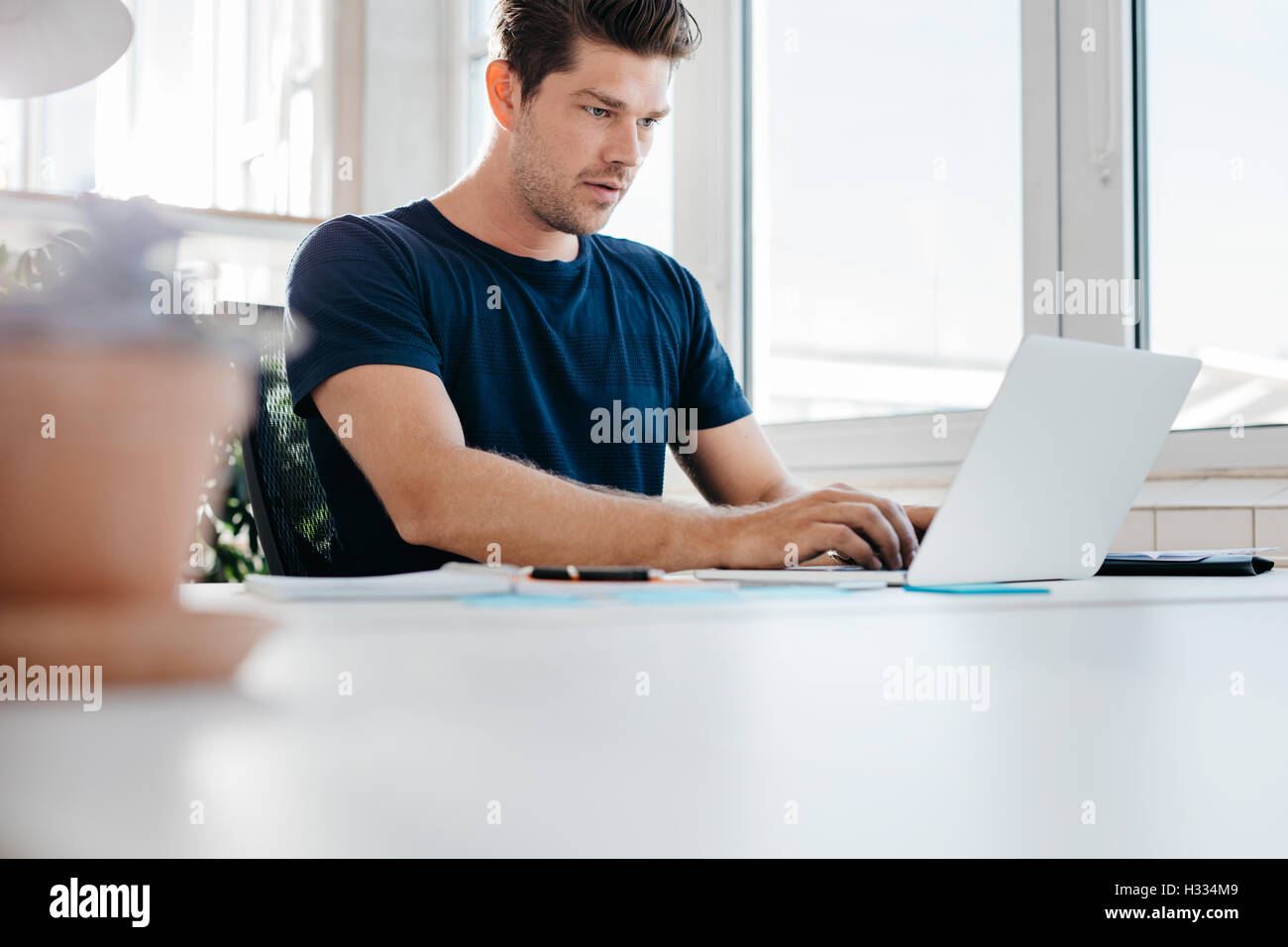 Busy young man working on laptop computer in office. Young male executive using laptop at his desk. Stock Photo