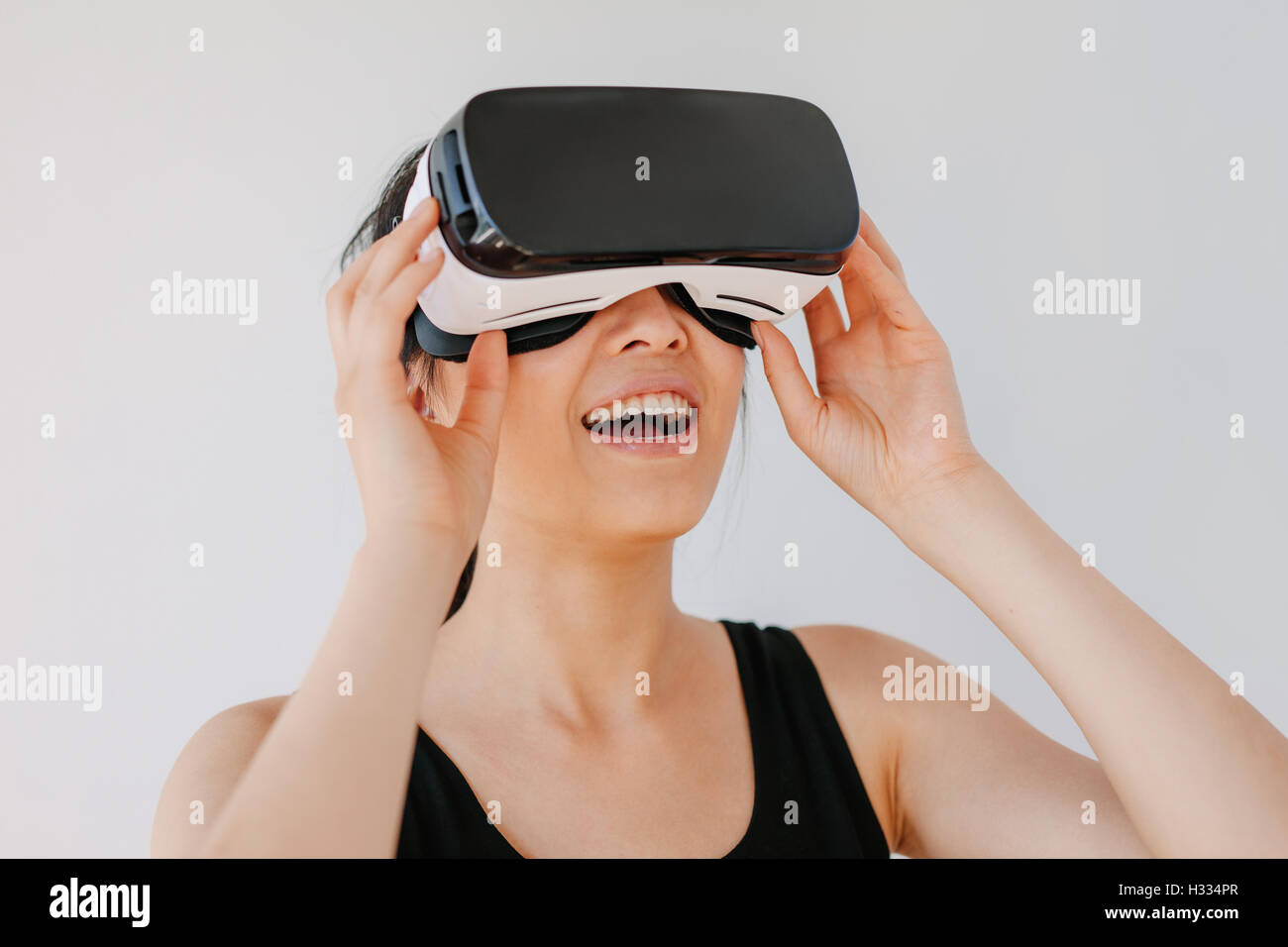 Close up of happy young woman using the VR goggles against grey background. Asian female model wearing virtual reality headset. Stock Photo