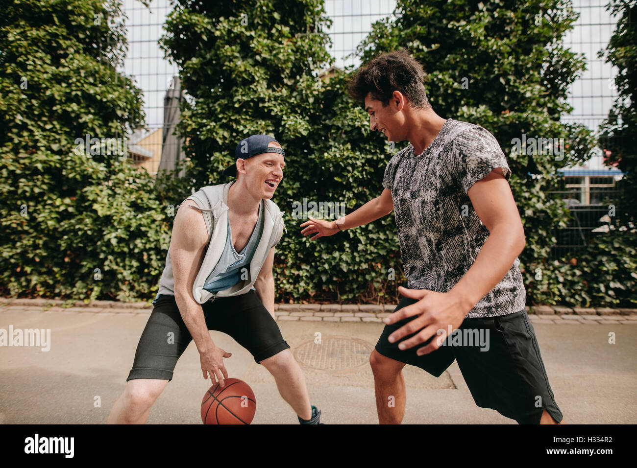 Two young men on basketball court dribbling with ball. Friends playing basketball on court and having fun. Stock Photo