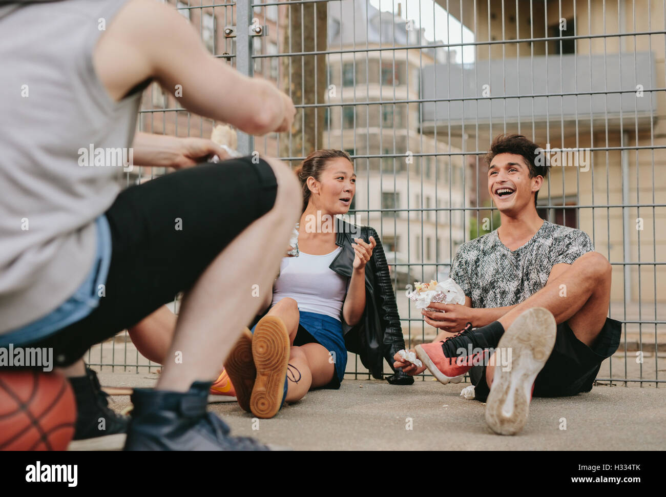 Shot of young men and woman relaxing outdoors and having fun. Group of friends hanging out on basketball court. Stock Photo