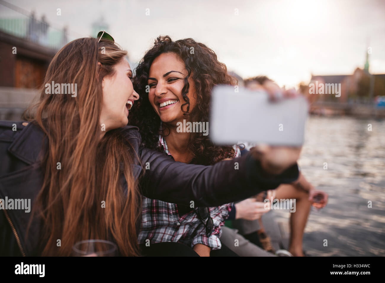 Cheerful young women friends taking selfie by the lake. Best friends having fun together. Stock Photo