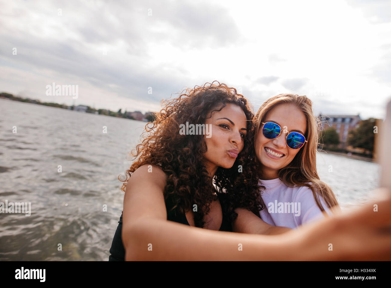 Shot of beautiful girls taking selfie with mobile phone by the lake. Young women posing for self portrait. Stock Photo