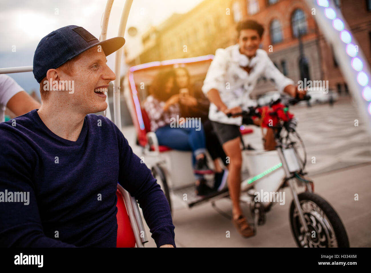 Happy young man enjoying tricycle ride in the city with friends. Teenagers enjoying holiday on tricycles. Stock Photo