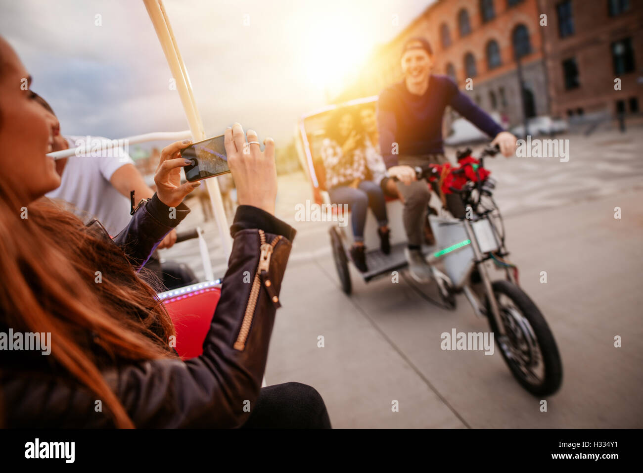 Woman photographing friends on tricycle ride. Teenagers having fun on vacation. Stock Photo