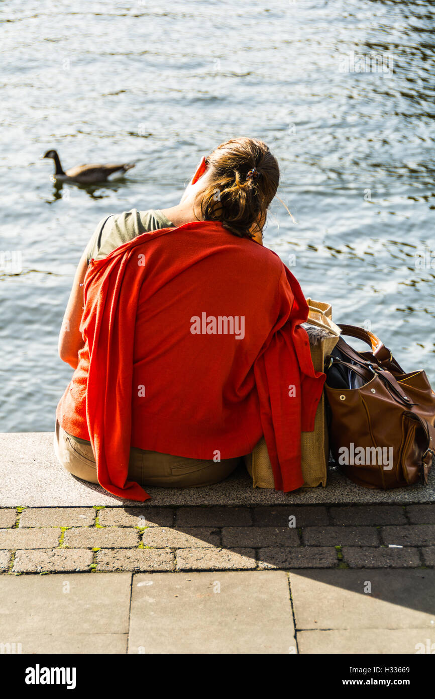 A tired looking woman sitting on the banks of the River Thames, London, England, UK Stock Photo