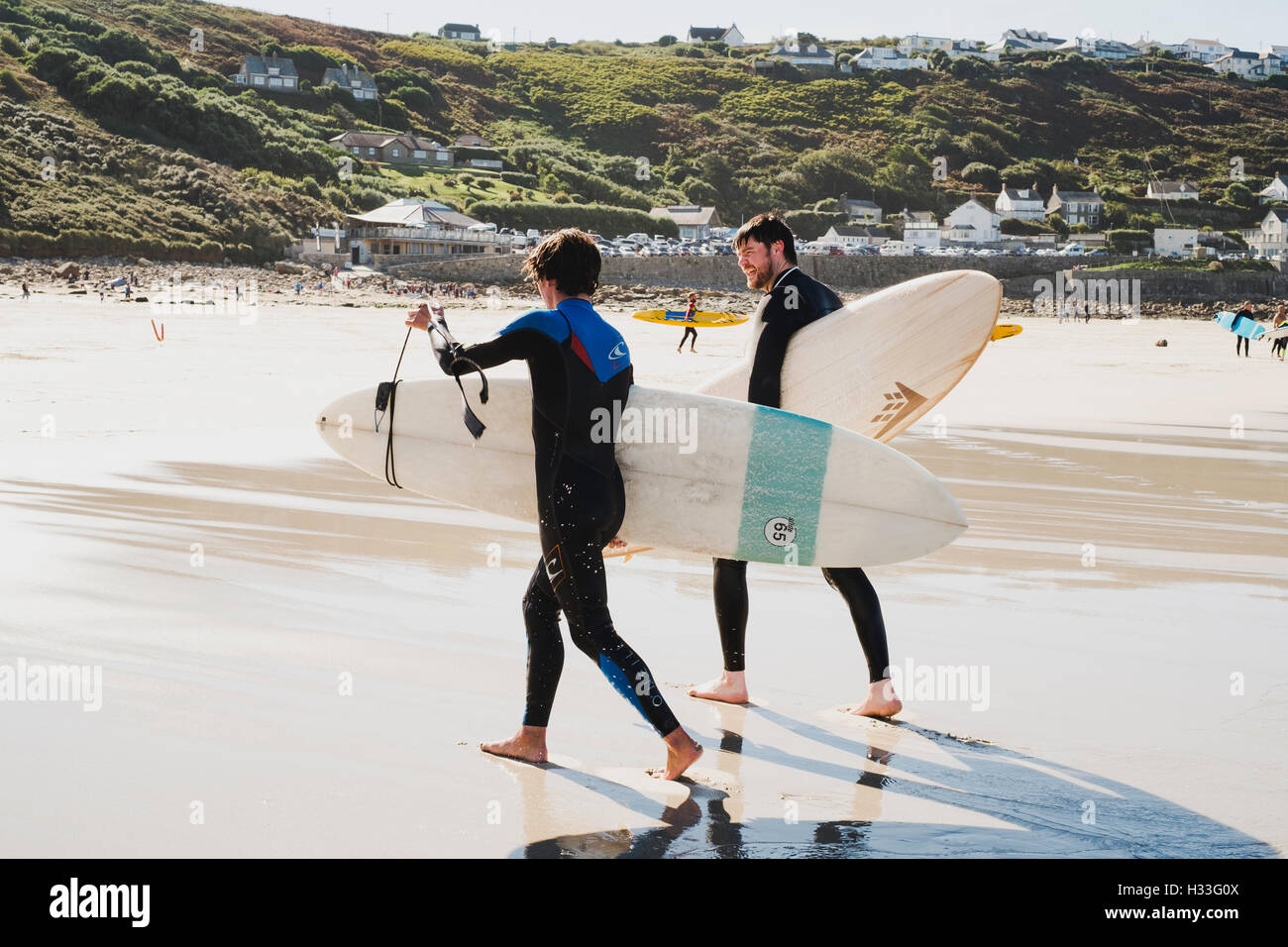 Two young men carrying the boards up the beach after surfing at Sennen Cove, Cornwall Stock Photo