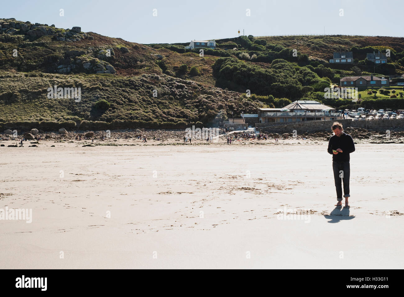 A lone man checking his phone on the beach at Sennen Cove, Cornwall Stock Photo