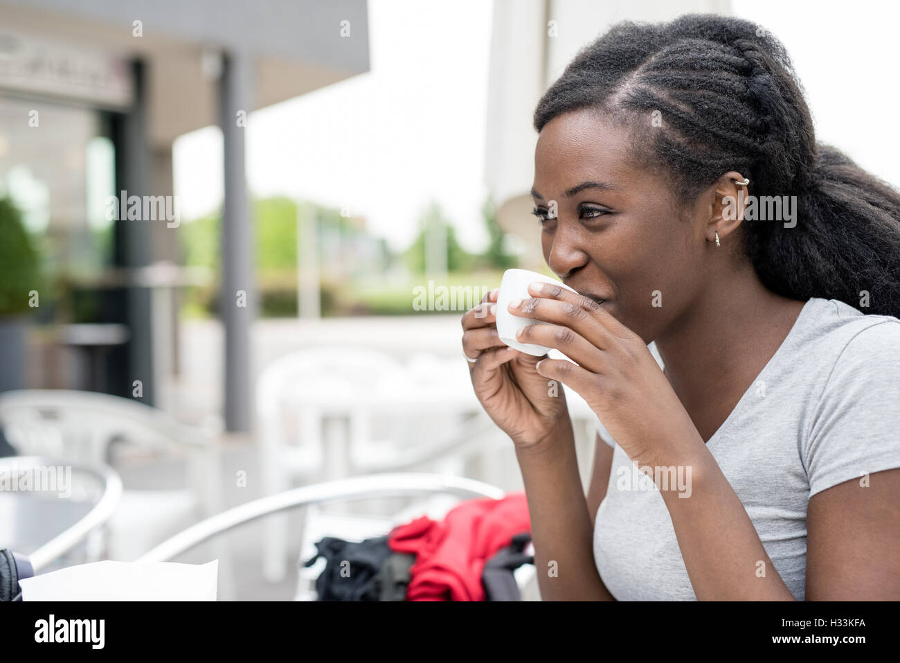 Young black woman having a cup of coffee outdoor in a bar, overlooking ...