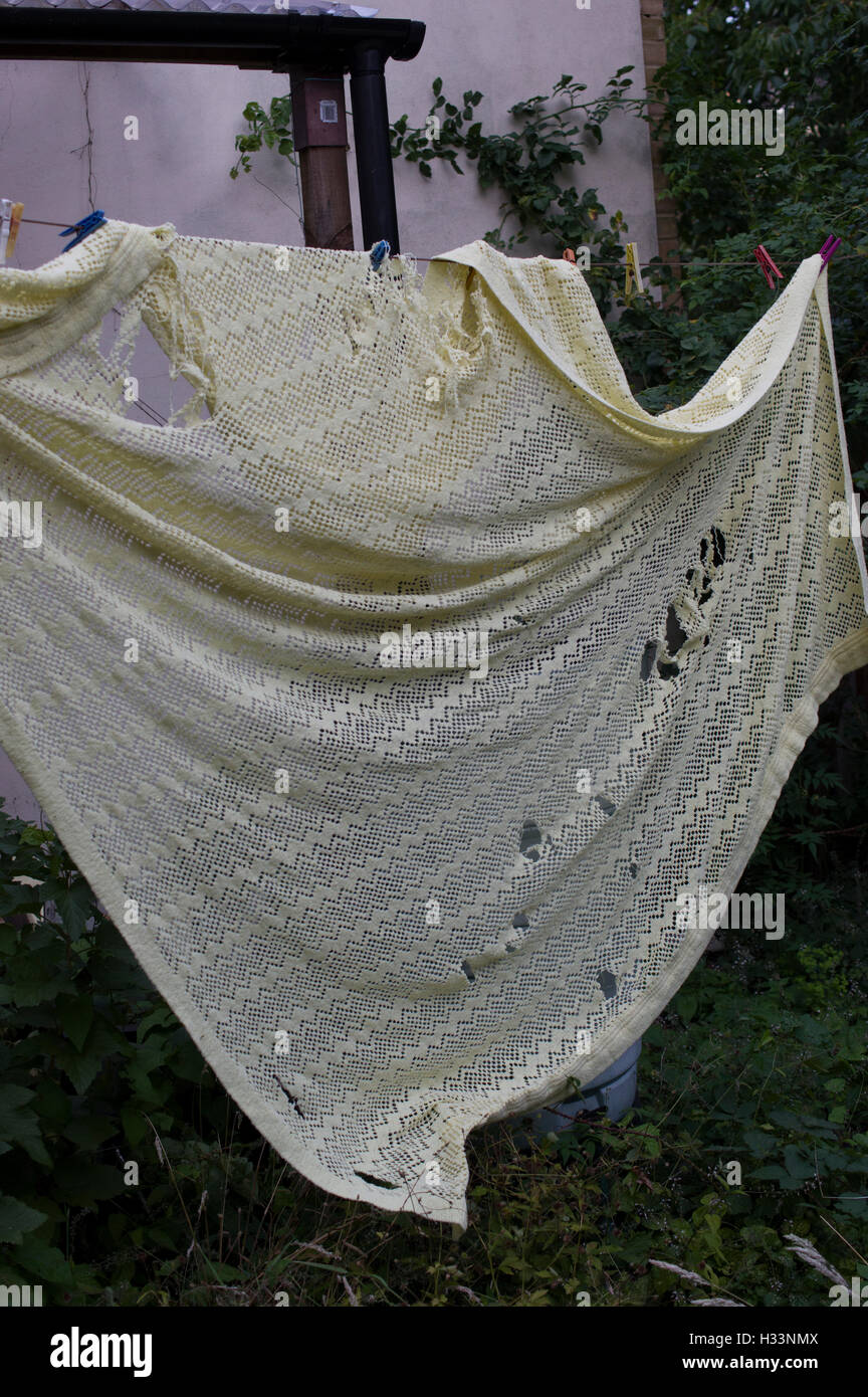 Tattered and moth eaten bedspread hanging from a washing line Stock Photo
