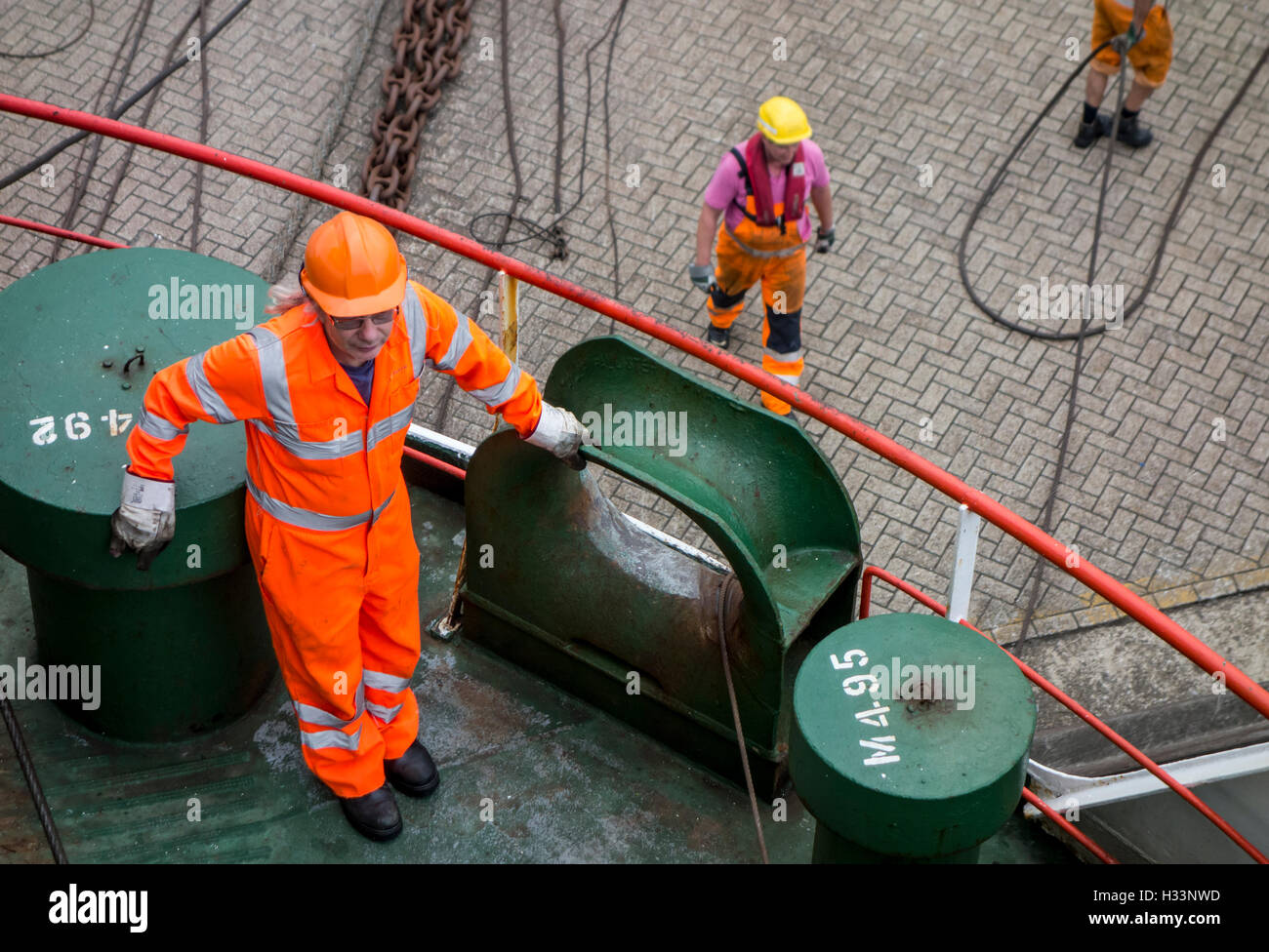 Ship's crew member in orange overall and dockworkers helping to moor ferry boat in seaport's dock Stock Photo