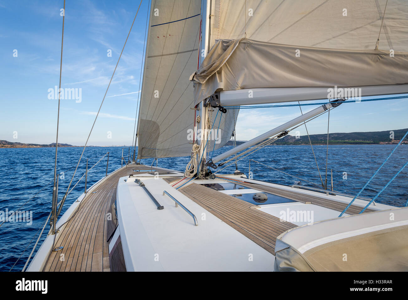 Sailing boat teak deck and hoisted sails, view from the cockpit to the